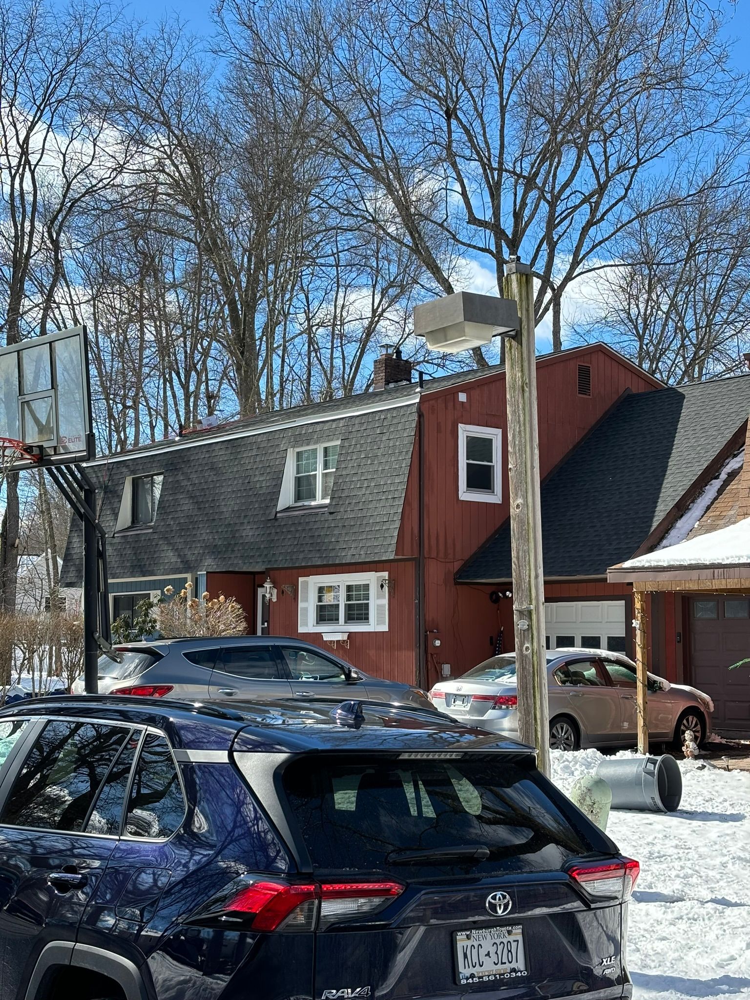 SUV parked in front of a red house with a basketball hoop in winter.