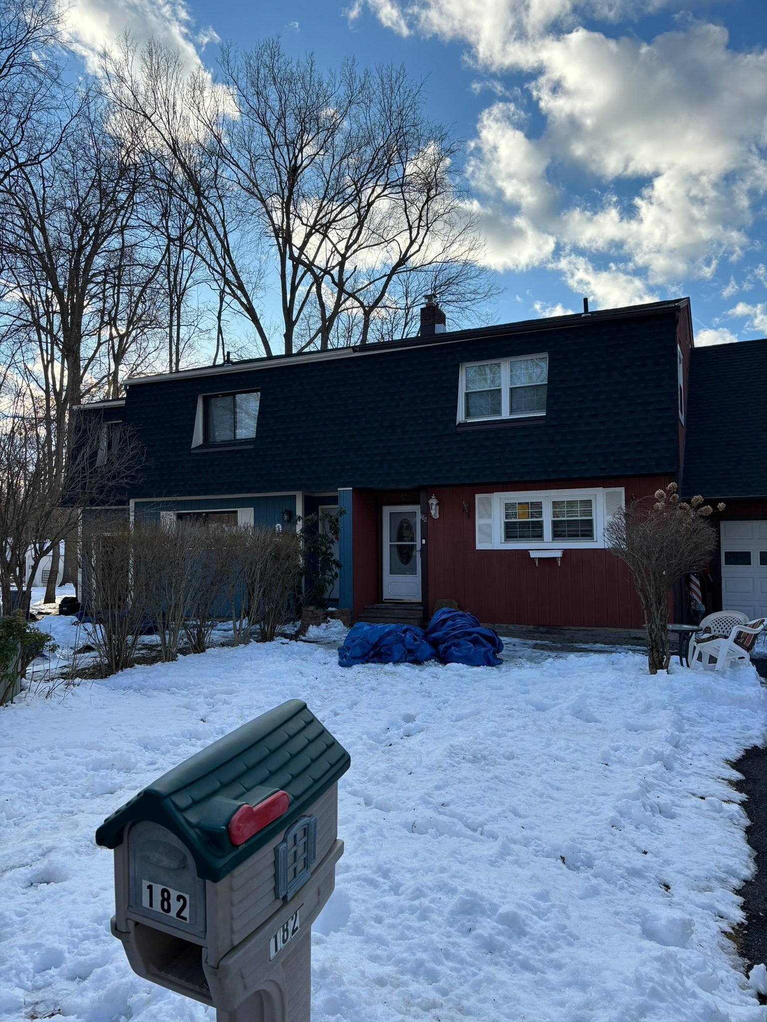 Snowy front yard with a house, green mailbox, and blue tarps on the porch.
