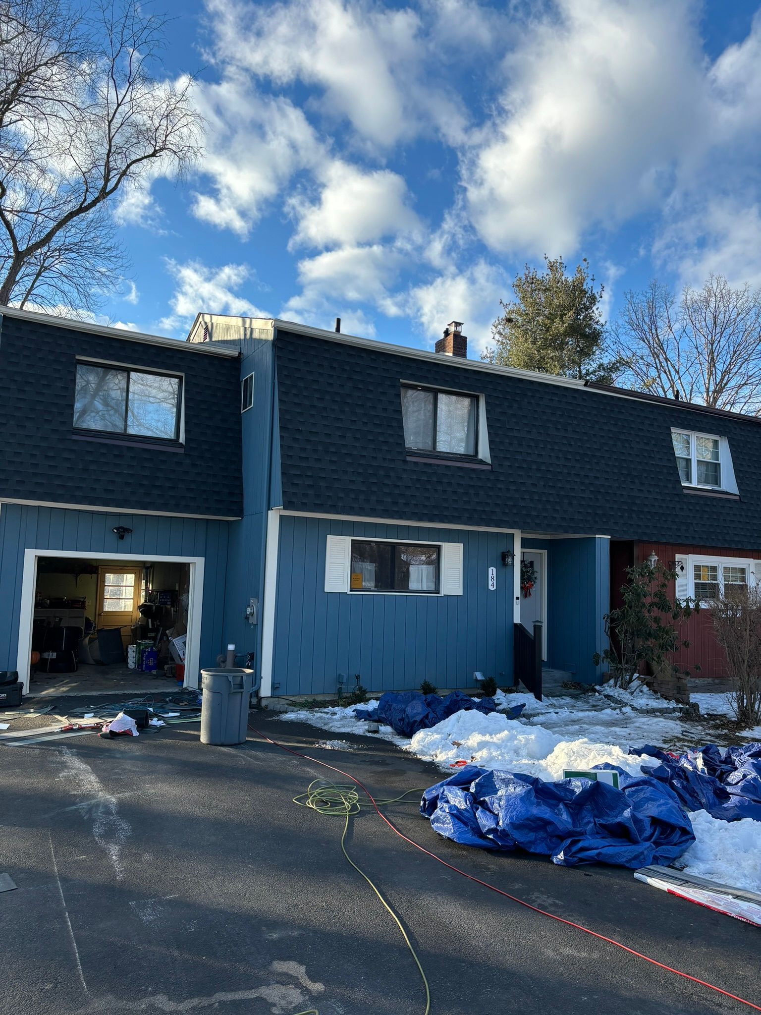 Blue townhouse under construction with snow and tarps on the ground.