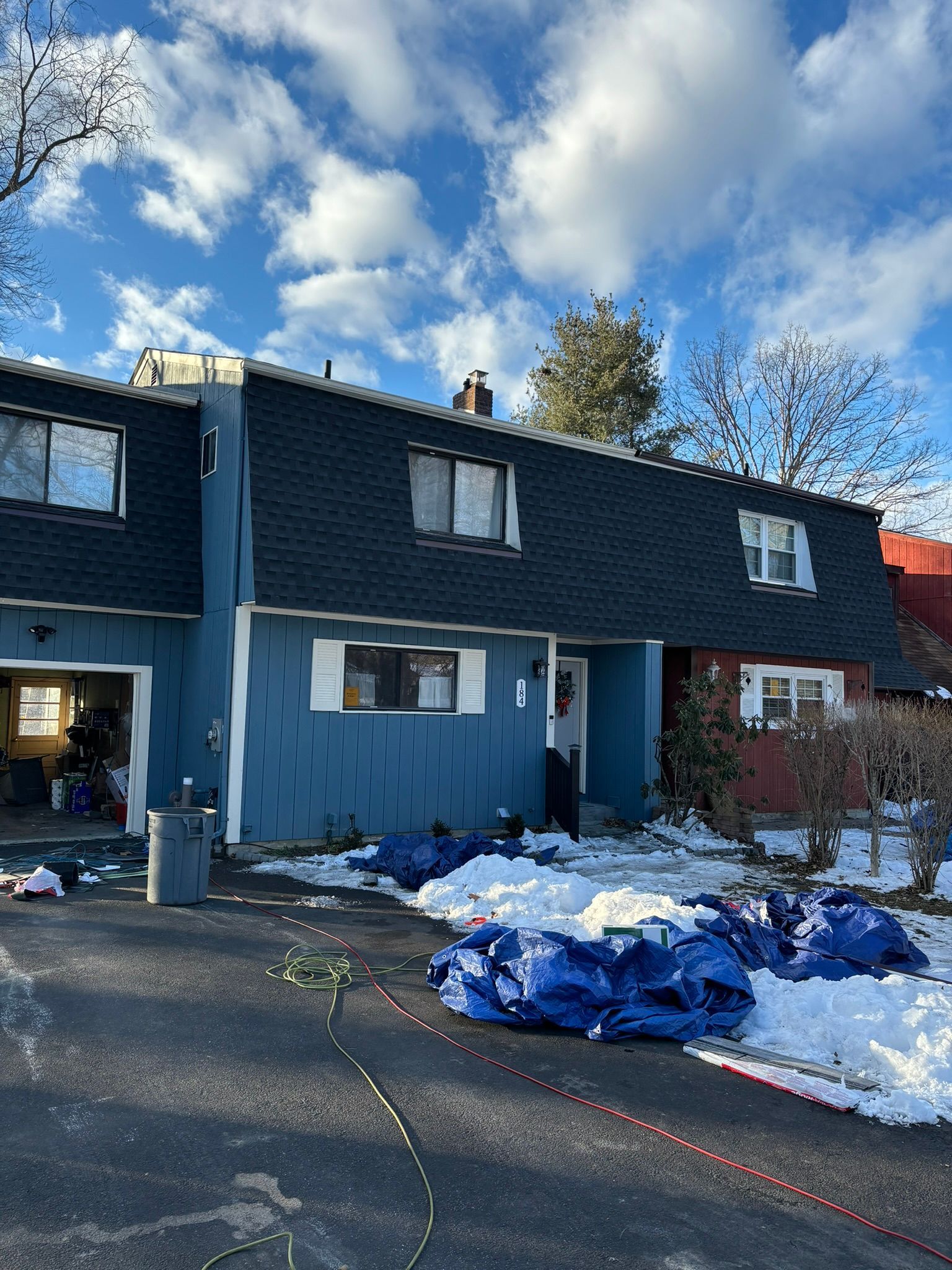 Blue townhouses with dark roofs and blue tarps in snow under a cloudy sky.