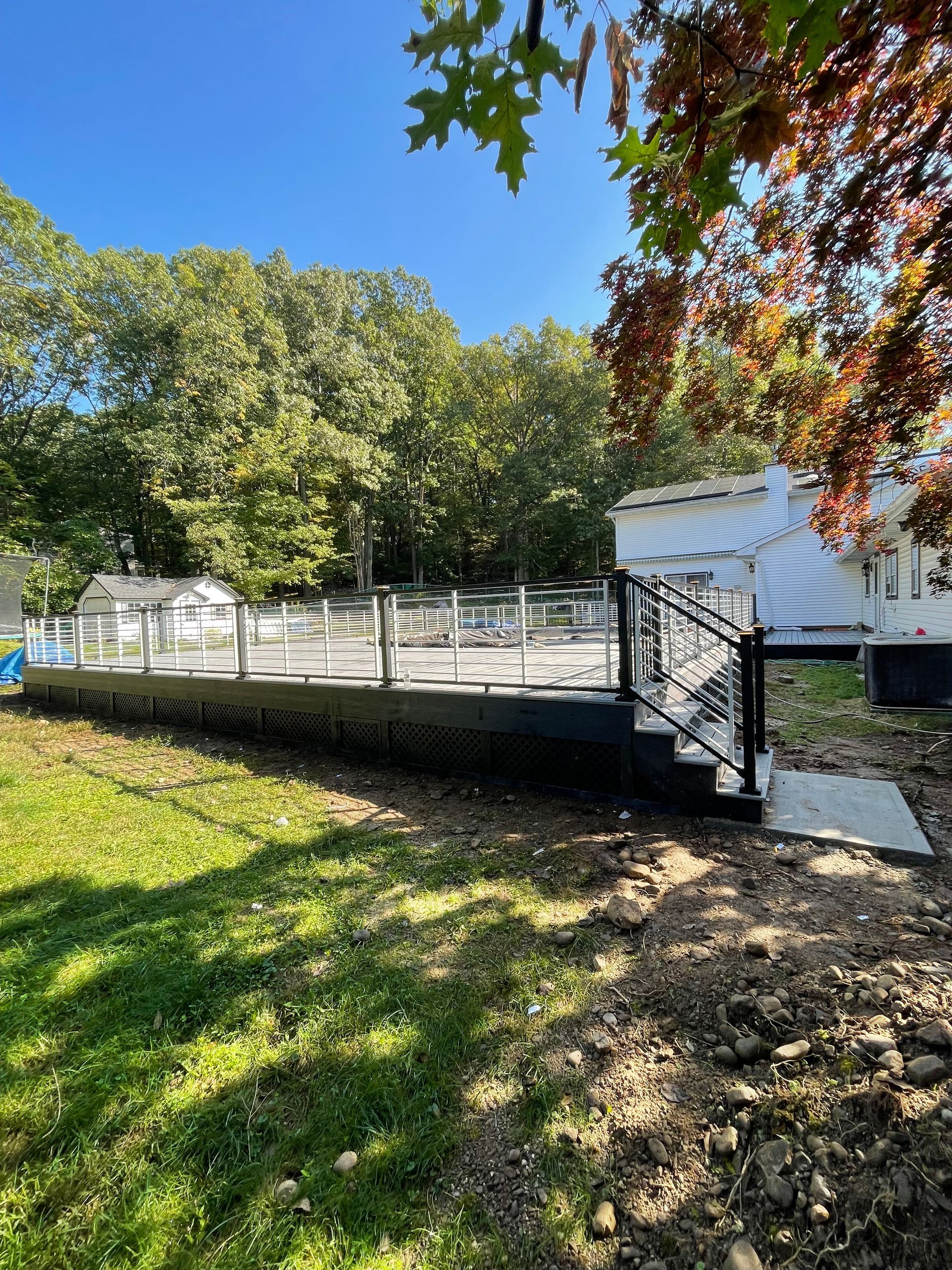 Black deck with glass railings next to a white building and green lawn, under a clear blue sky.