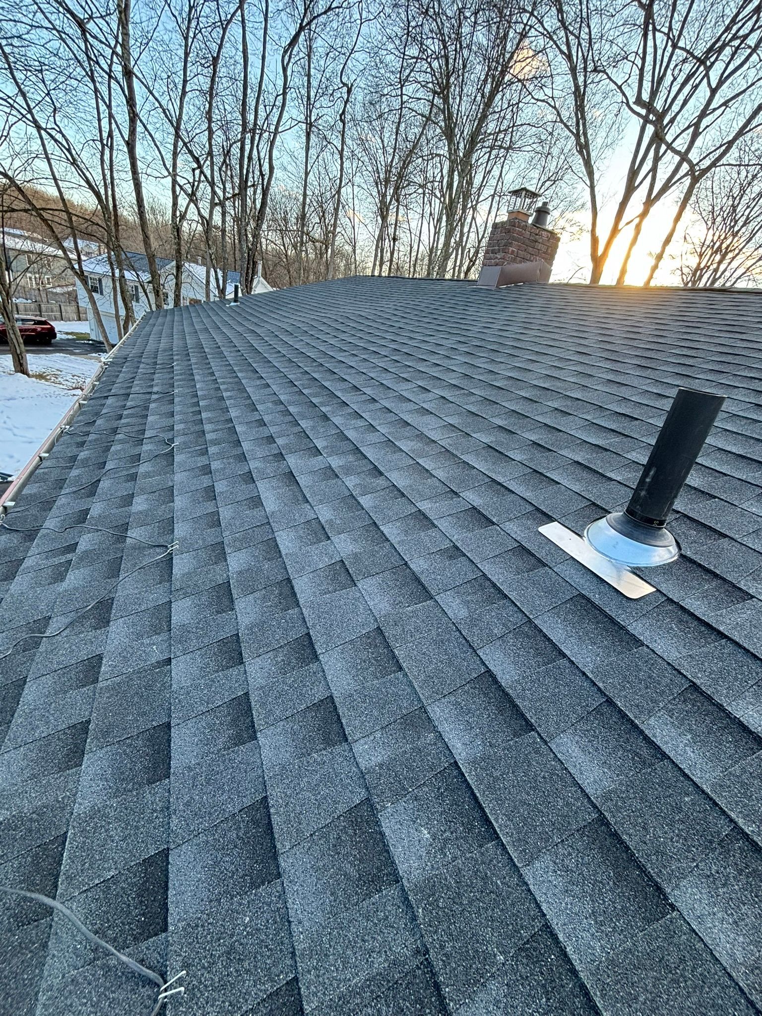 Gray shingled roof with vent and chimney against a wintery sky.