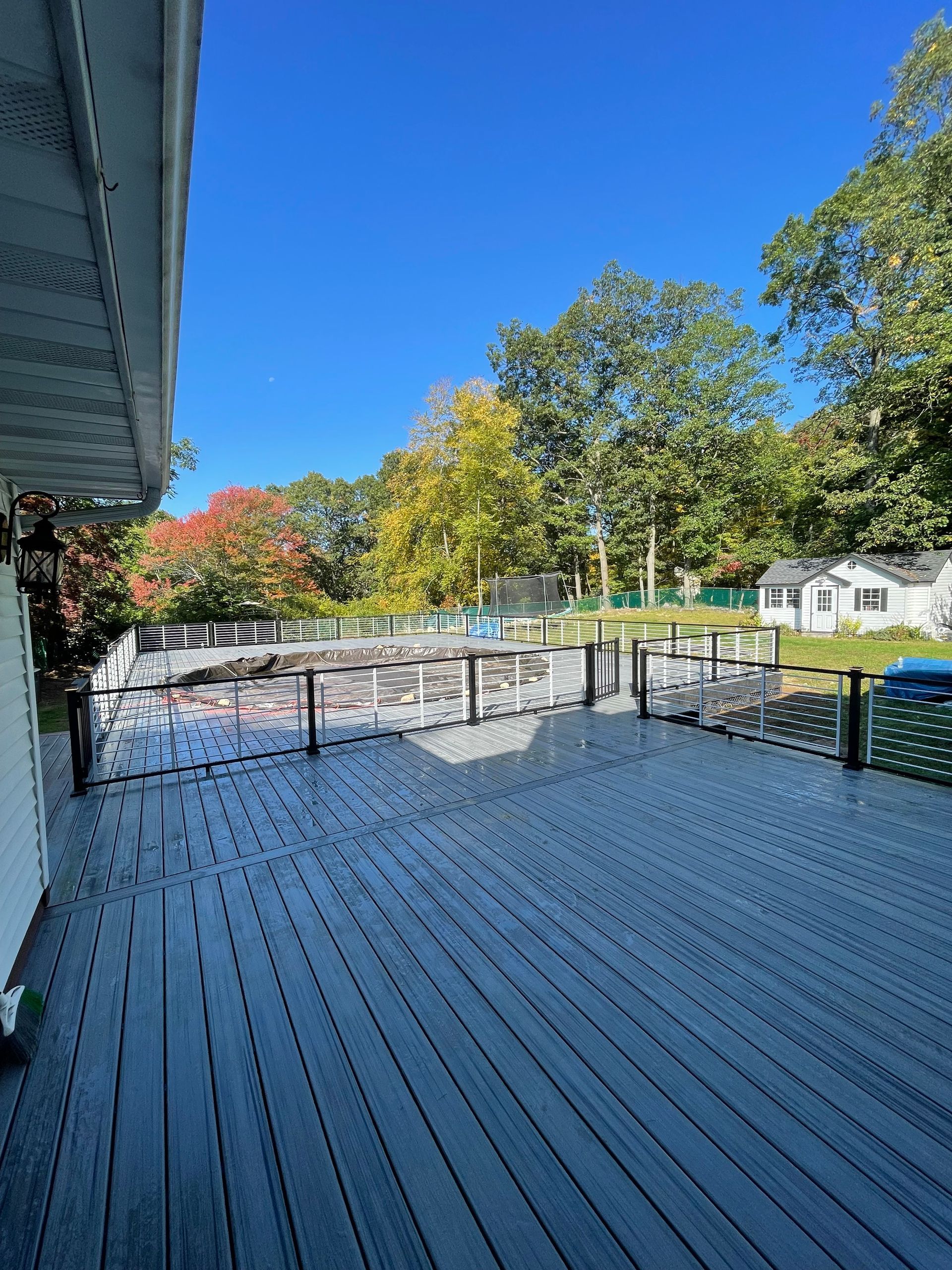 Wooden deck overlooks pool, lush trees, and small white buildings on a bright, sunny day.