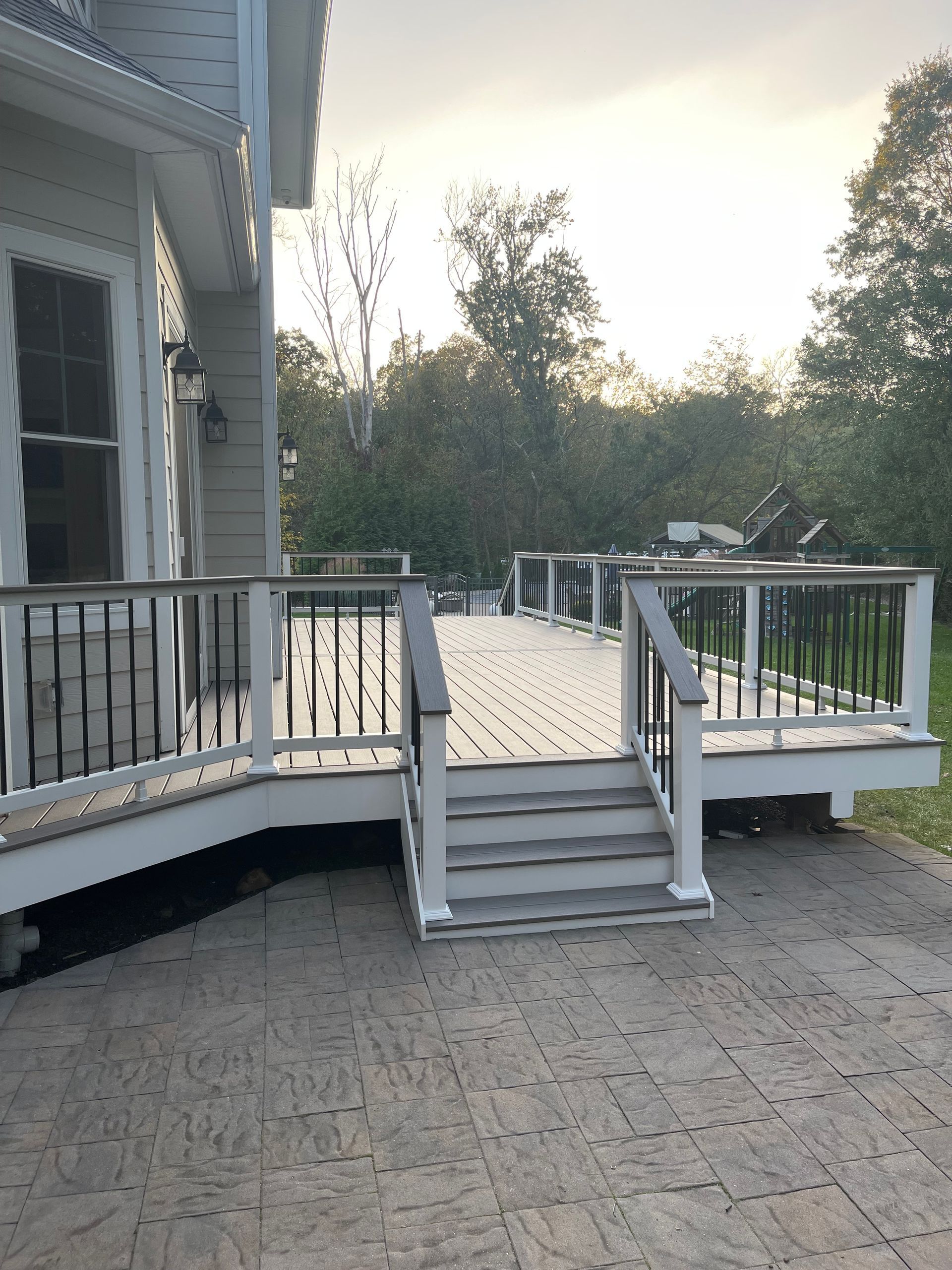 Deck with stairs, gray decking and railings, white posts, and black balusters, attached to a house.