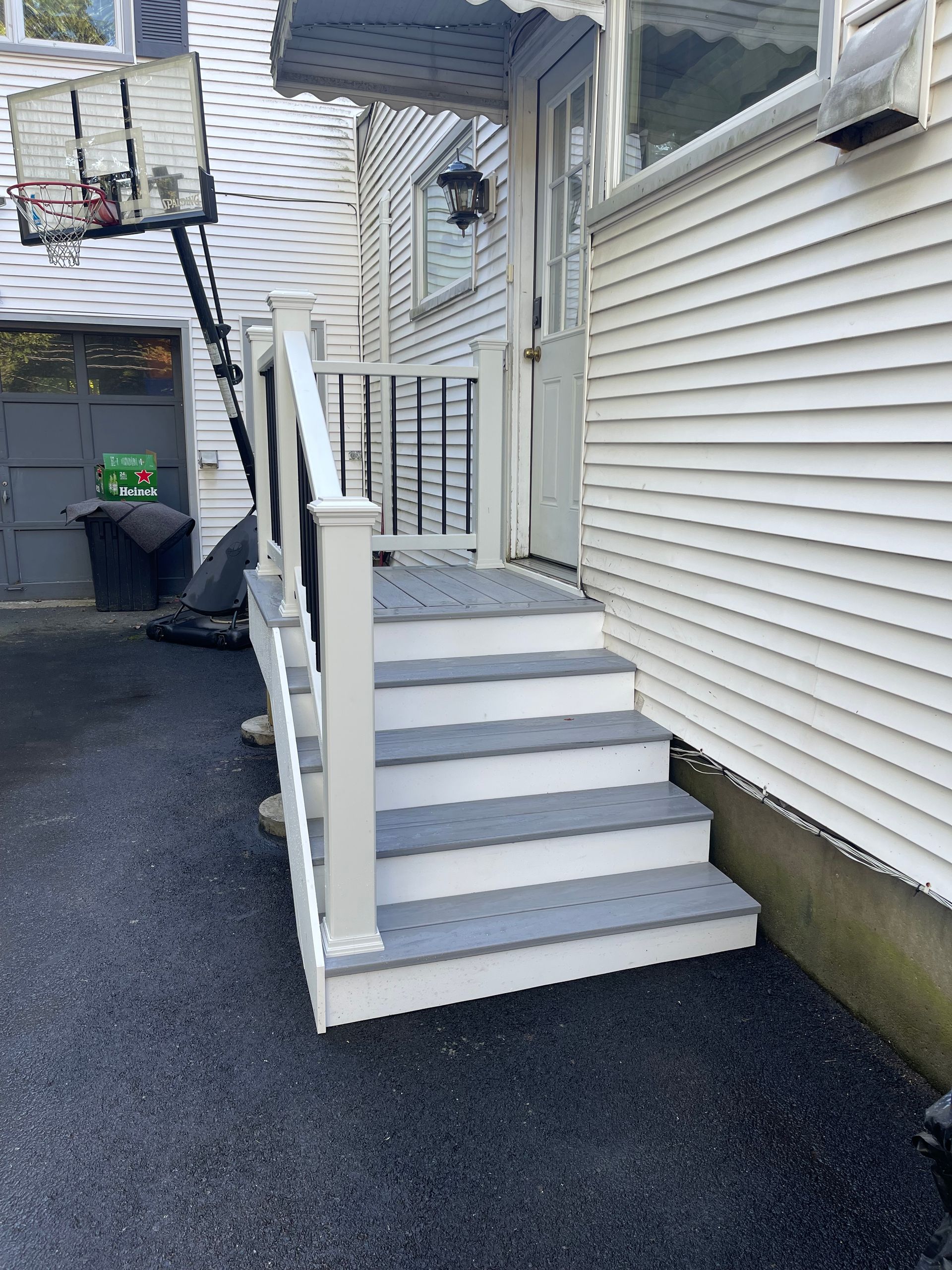 Gray steps leading up to a white-sided house entrance with a basketball hoop and asphalt driveway.