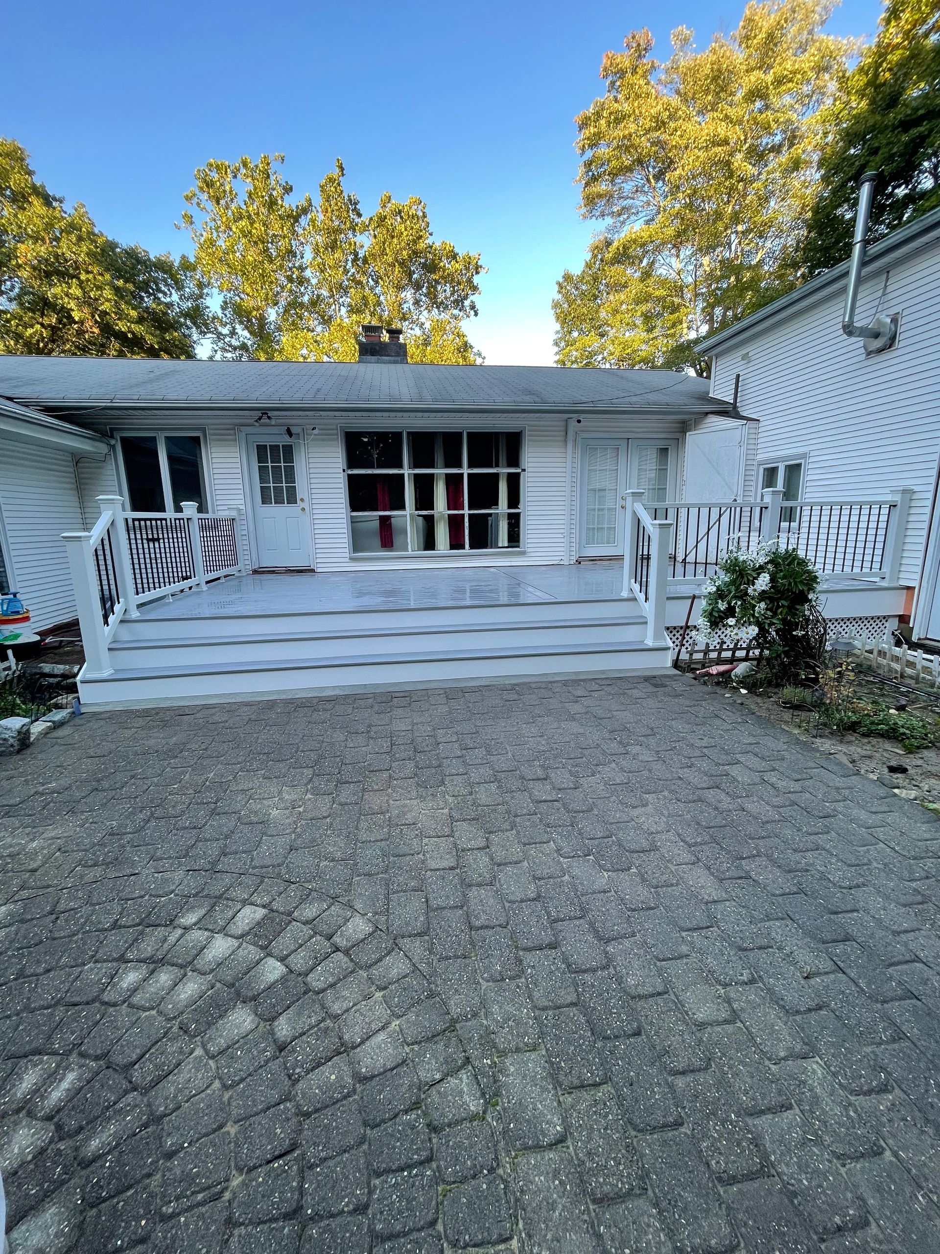 White house with steps, walkway, and zebra-striped railing. Paved driveway, trees in background.