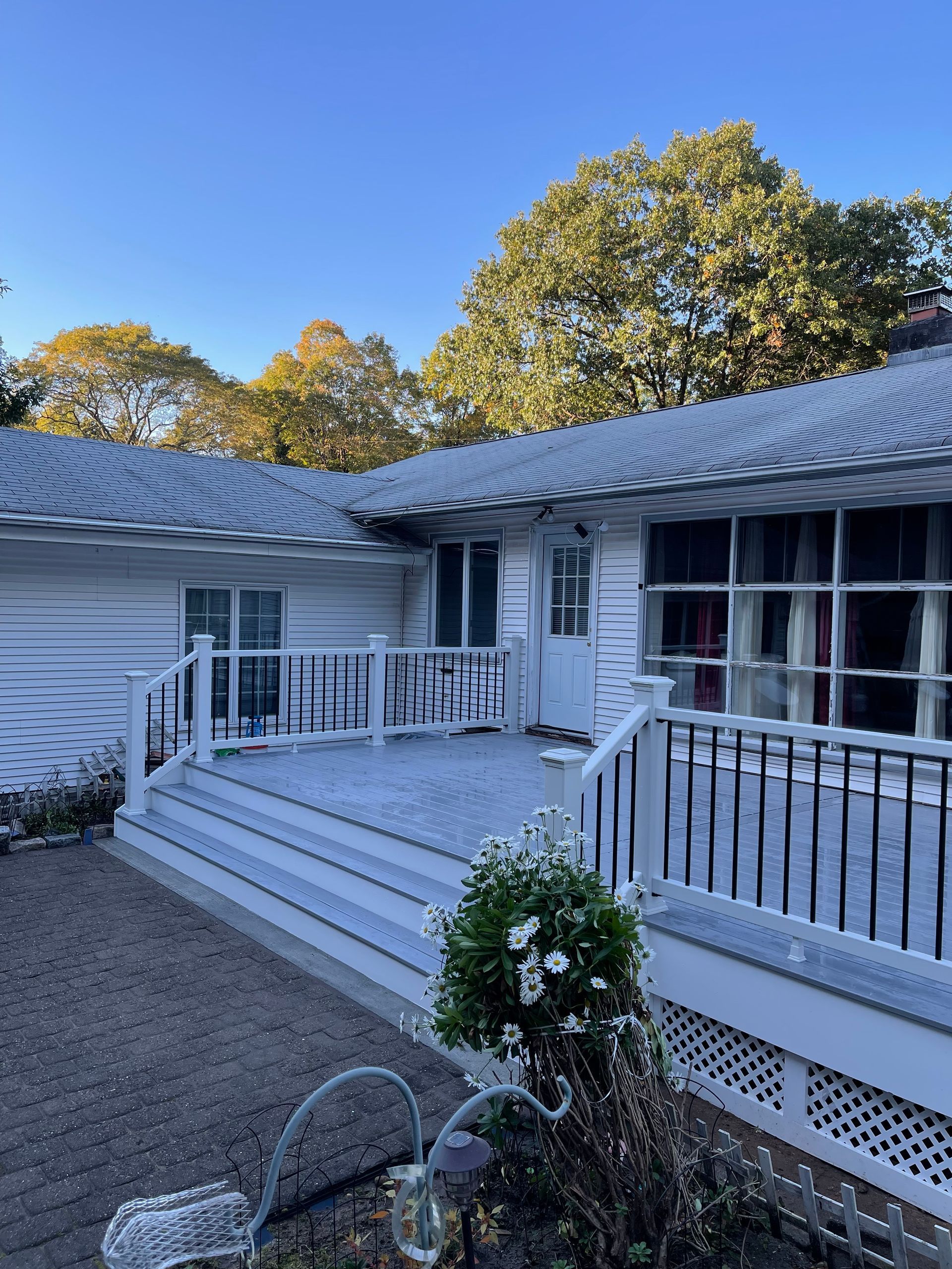 White house with deck, shrubs in front, gravel, sunny day.