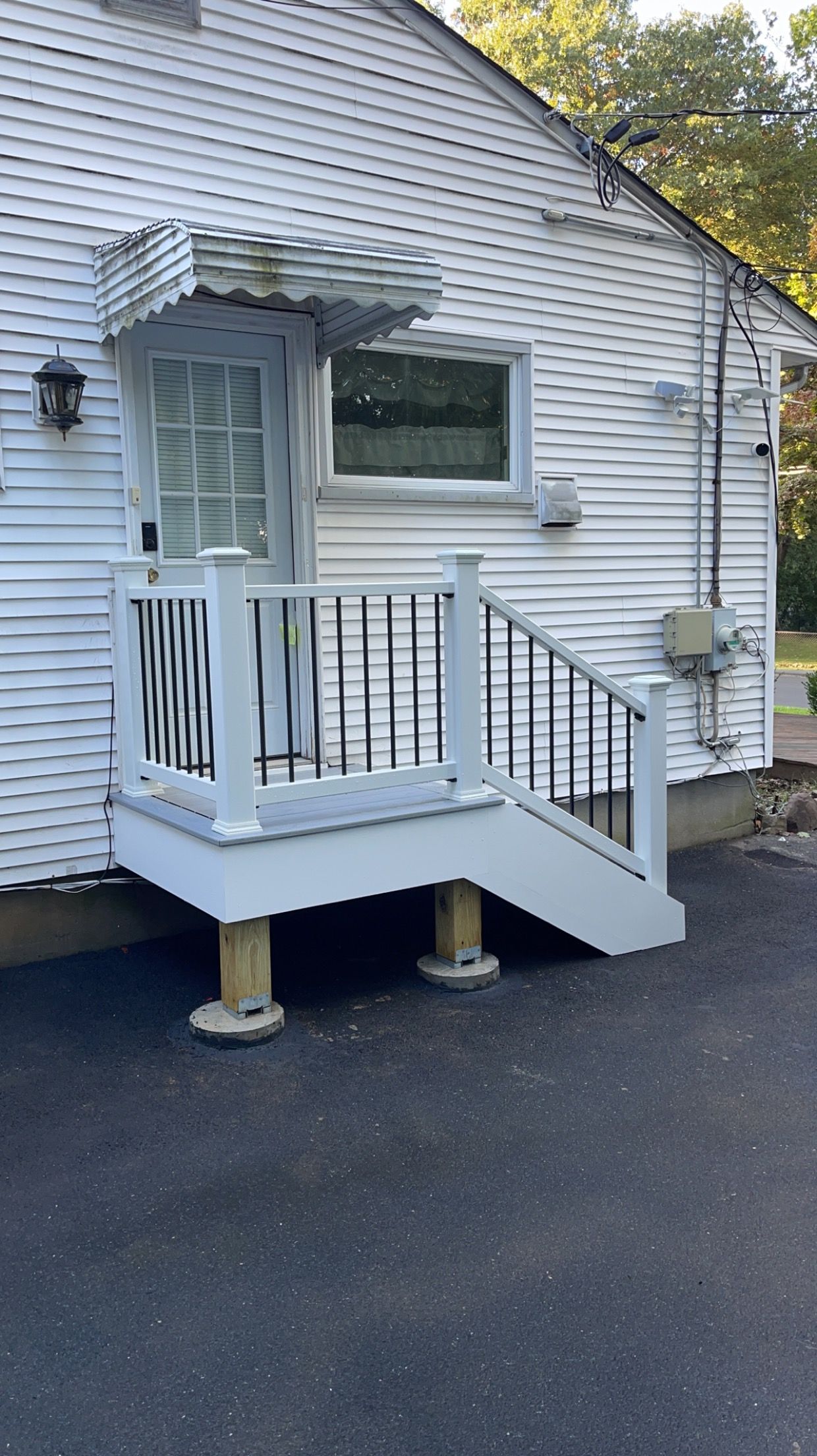 White house exterior with a raised porch, doorway with awning, and steps. Black asphalt driveway.