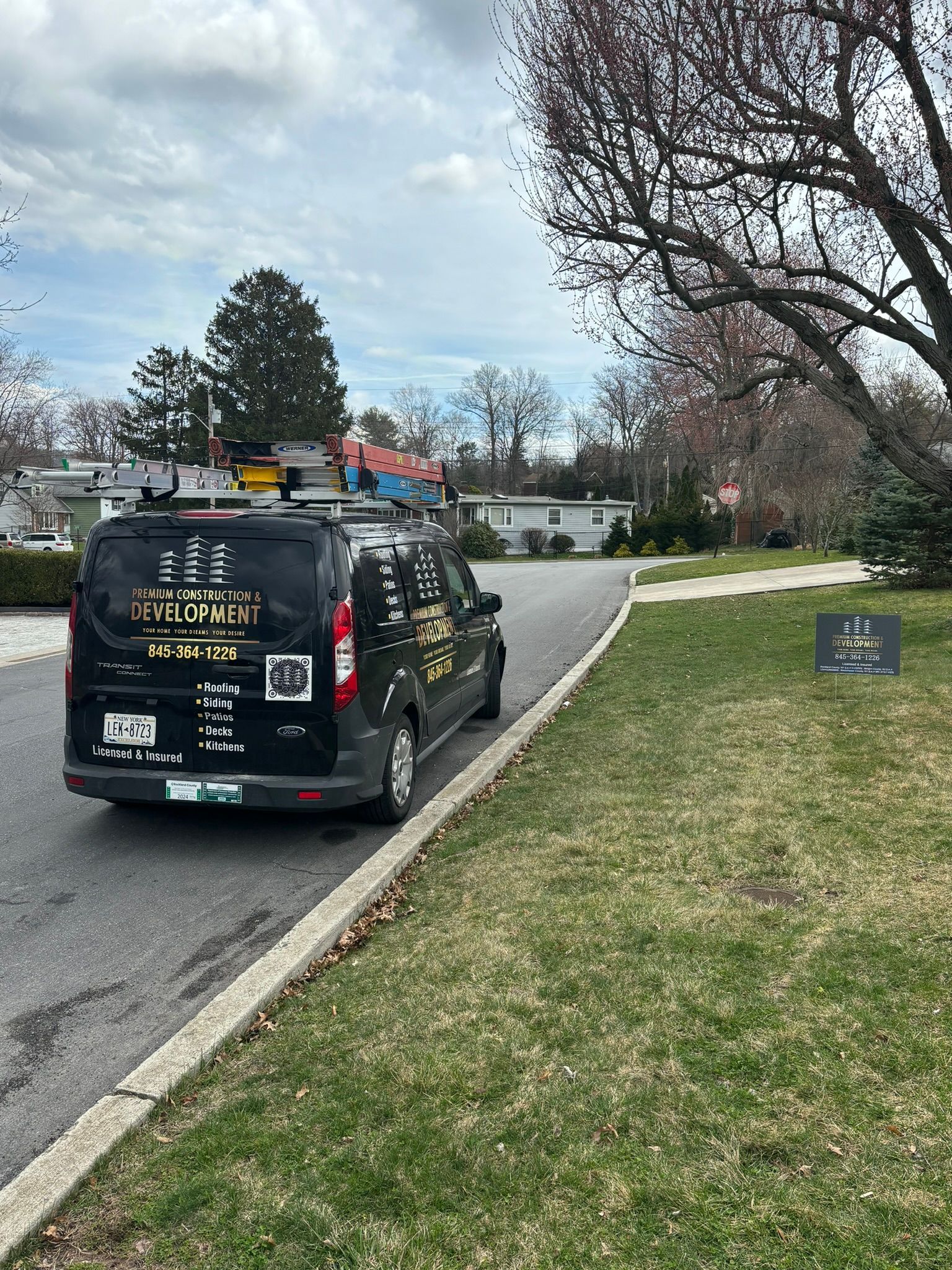Black service van parked on a residential street, with a lawn and trees on the right.