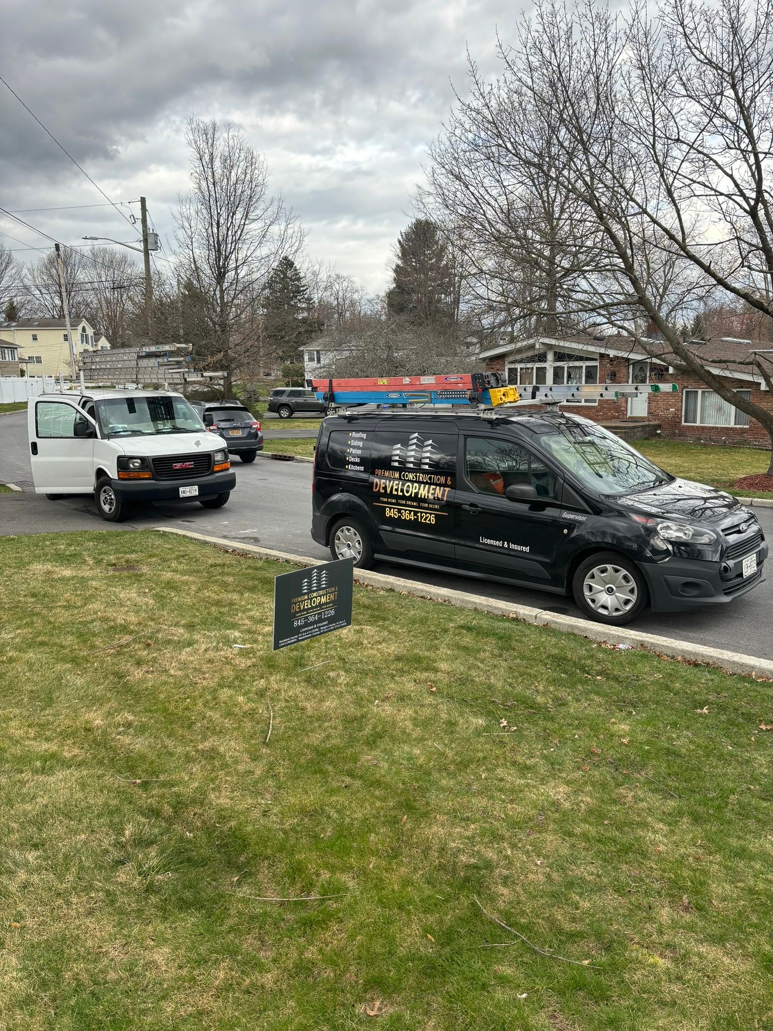 A black and white van parked on a lawn, other vehicles on the street, cloudy sky, residential area.