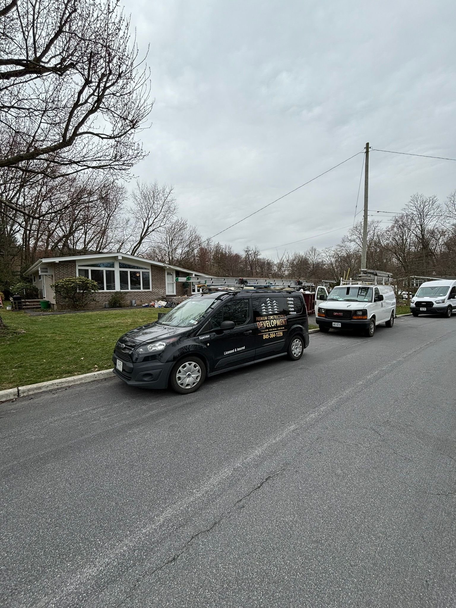 Black van parked on street in front of a house, two other vans in the background on a cloudy day.