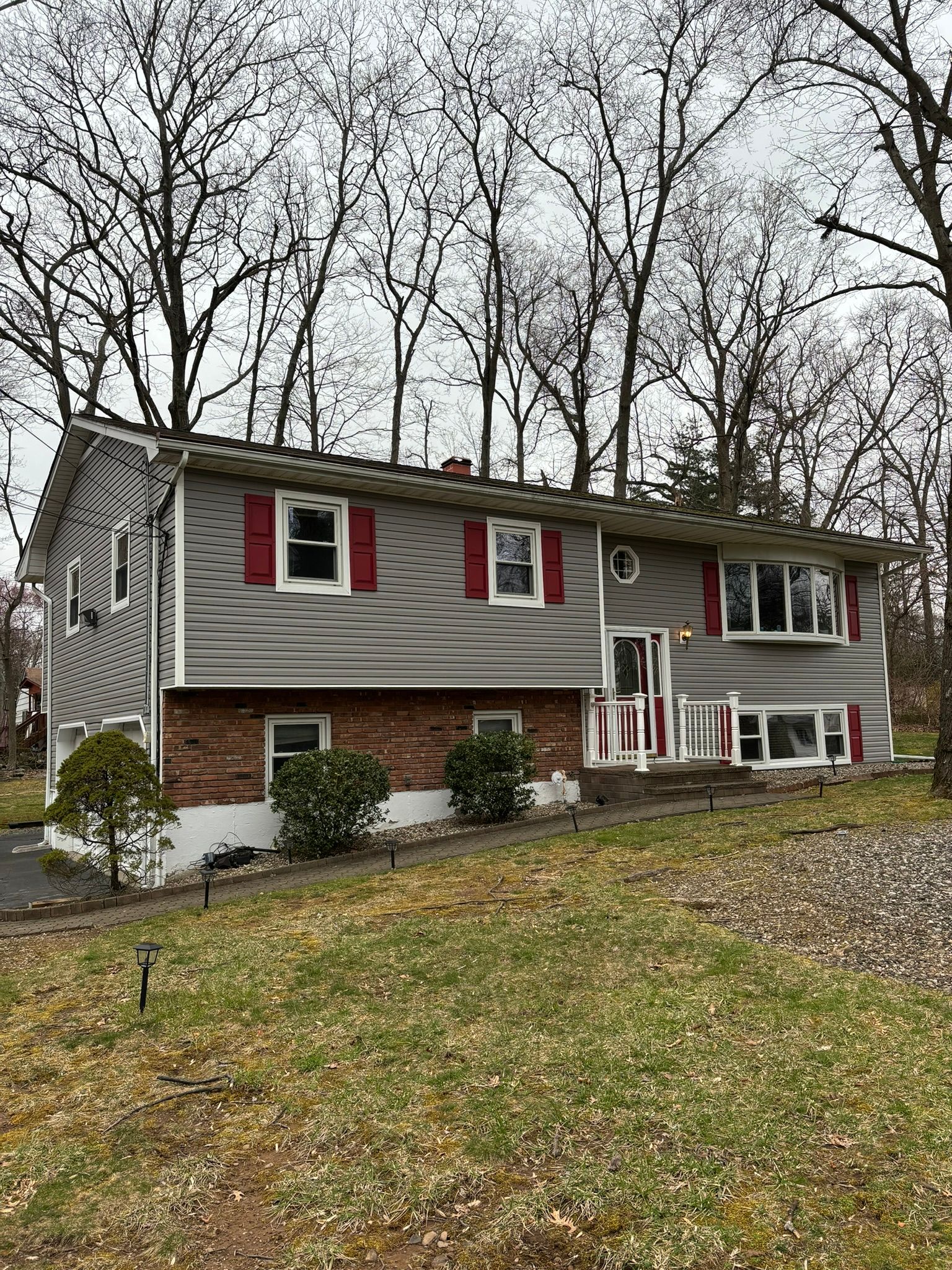 Two-story house with gray siding, red shutters, brick facade, and a grassy yard.