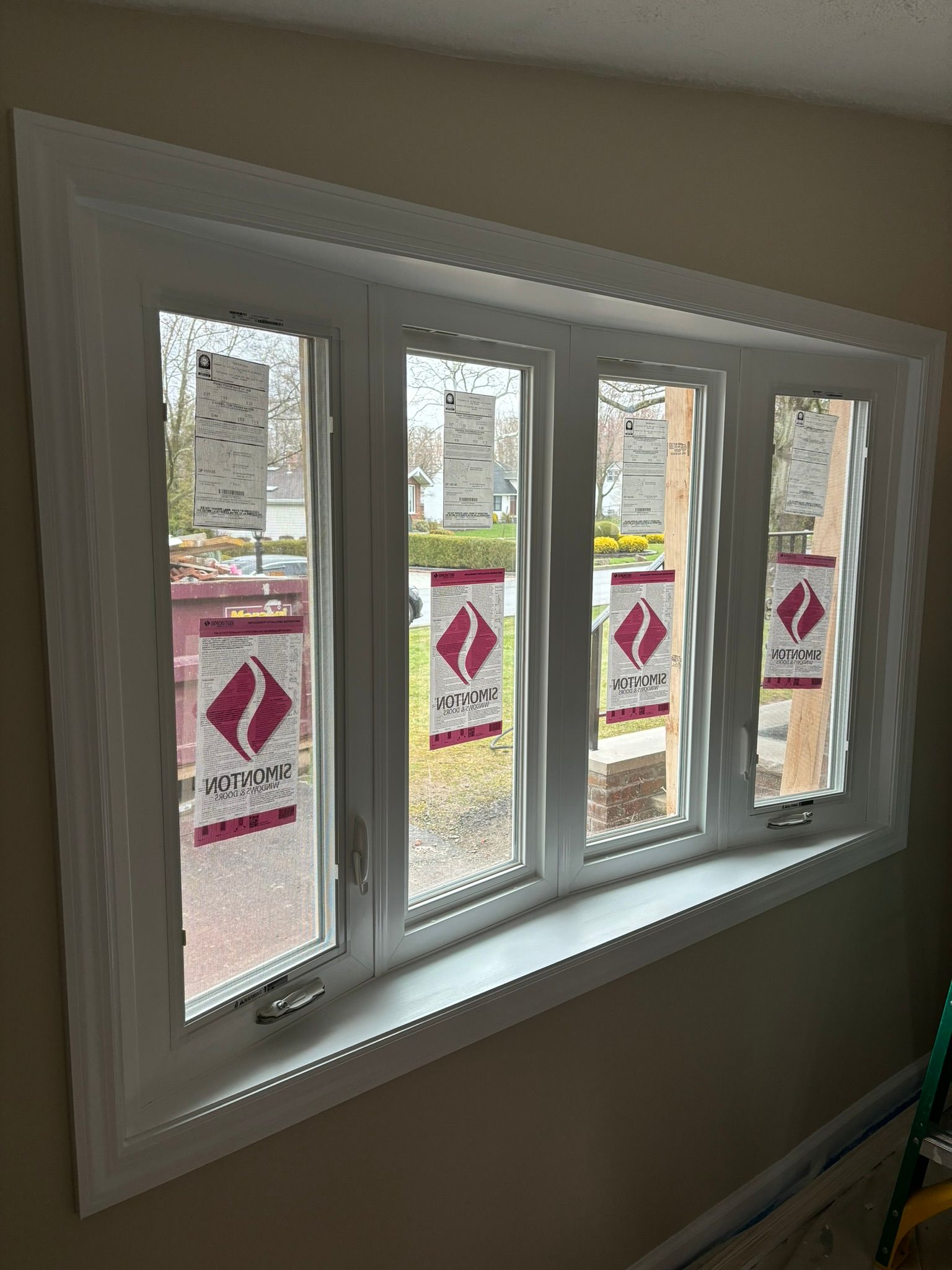 White-framed bay window with protective stickers, inside a room with beige walls.