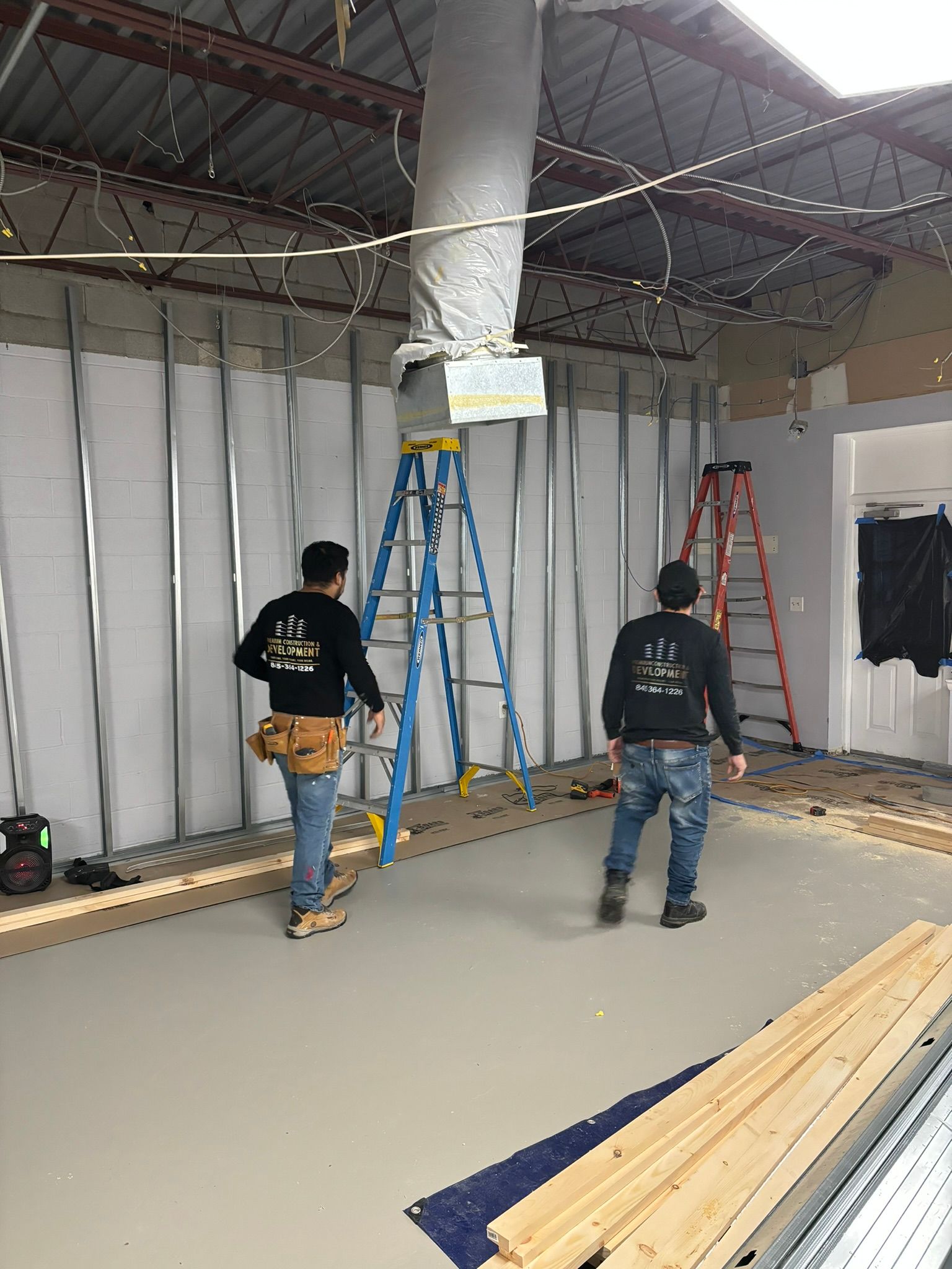 Two construction workers inside a building under renovation, framed walls and materials visible.