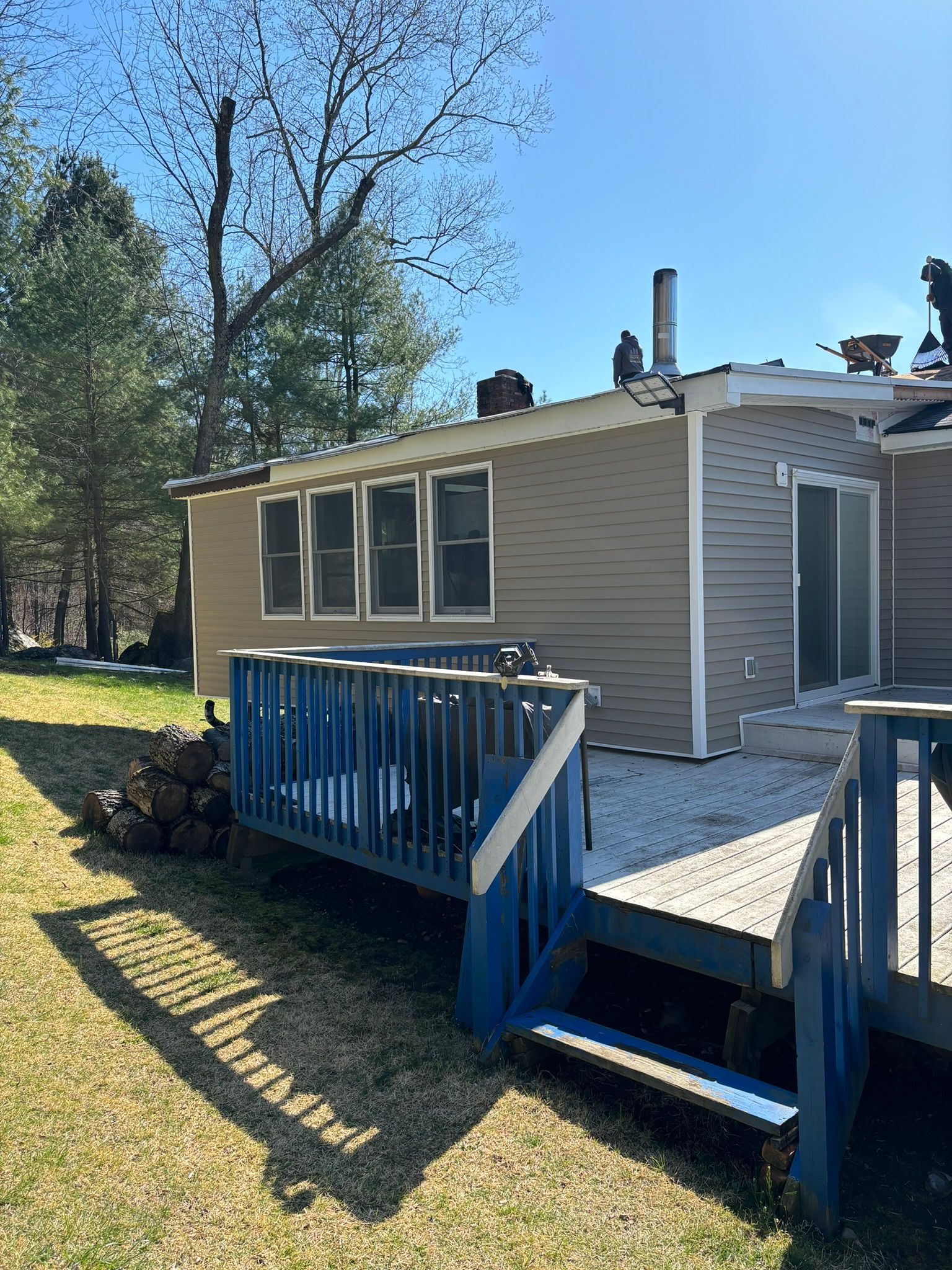 A deck with blue railing, next to a tan house with windows. Sunny day, outdoor setting.