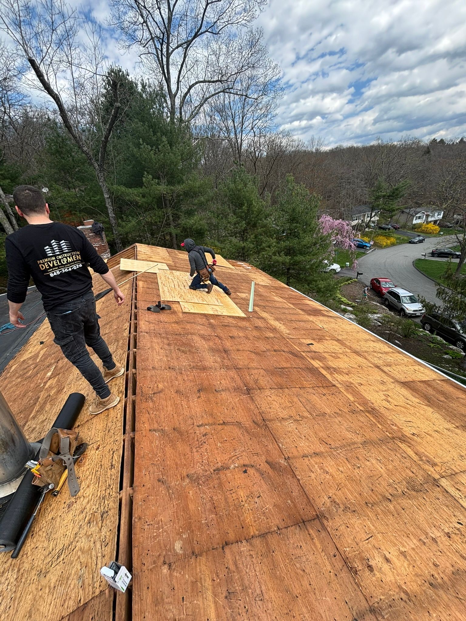 Two roofers working on a rooftop. A partly built roof with trees and houses in the background.