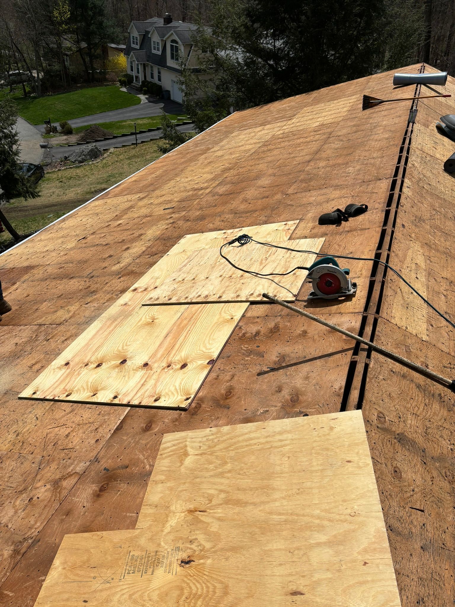 Roofer on a roof. A circular saw on plywood, surrounded by shingles being replaced. Daytime, outdoor.