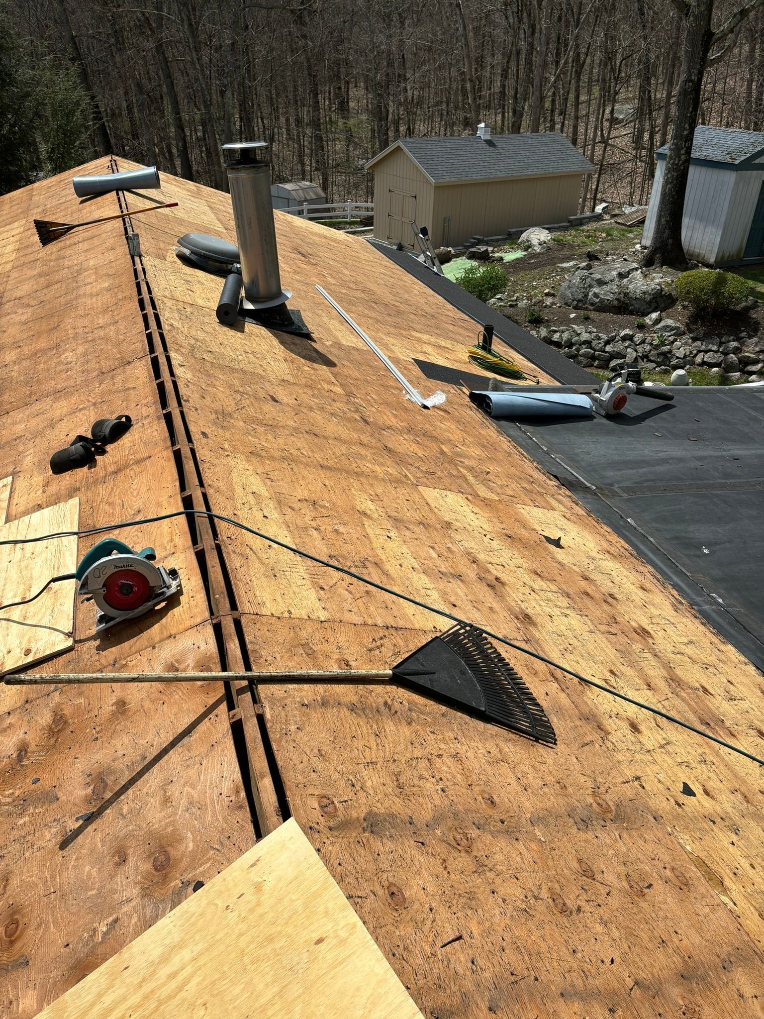 Roof partially stripped, with tools and debris. Chimney, small shed, and trees in the background.