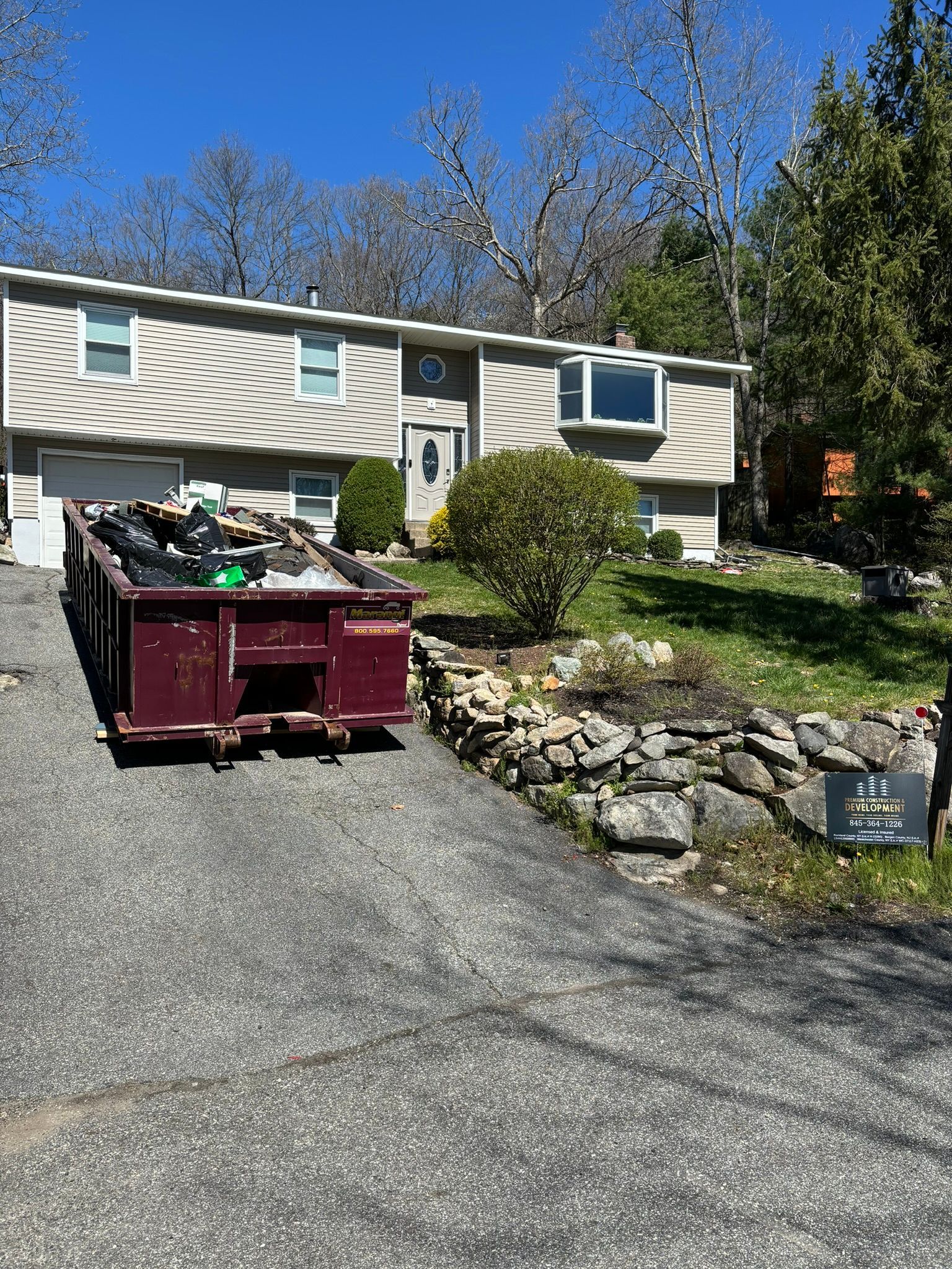 A house with a dumpster in the driveway, and stone wall.