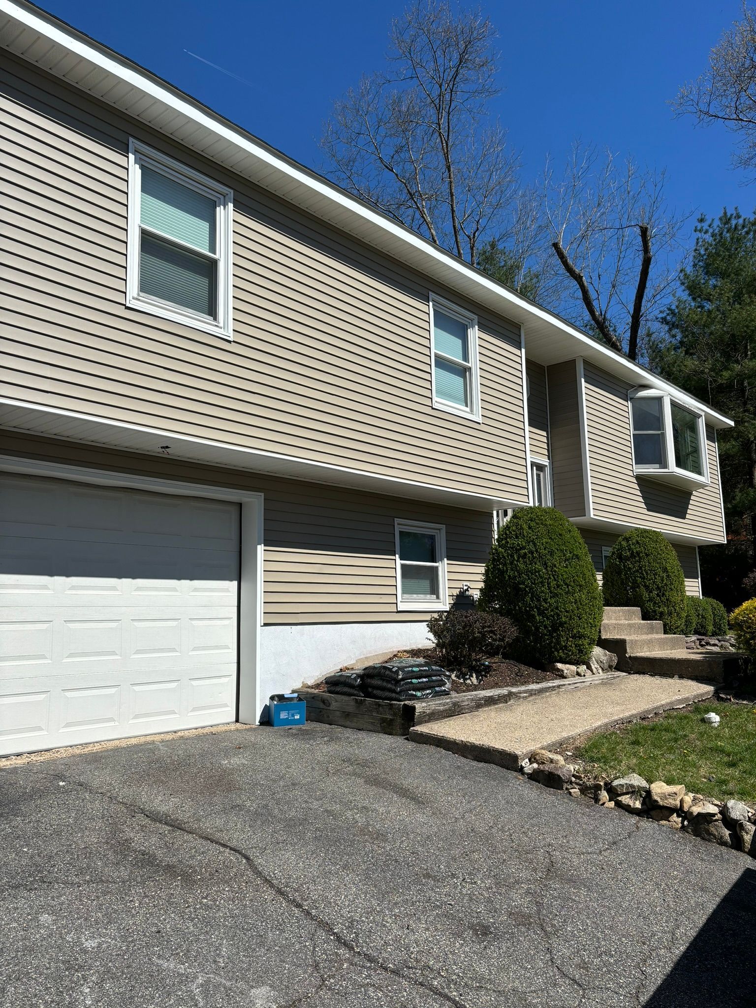 Two-story house with beige siding, white trim, and a driveway on a sunny day.