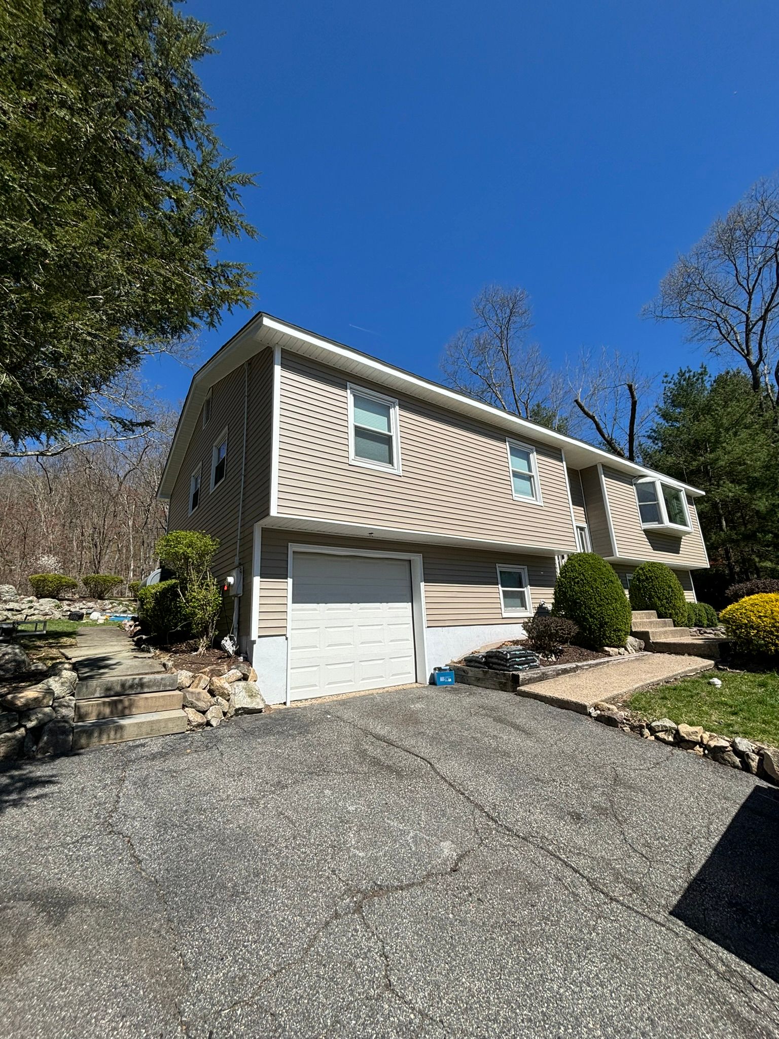 Tan two-story house with gray siding and a white garage door on a sunny day.