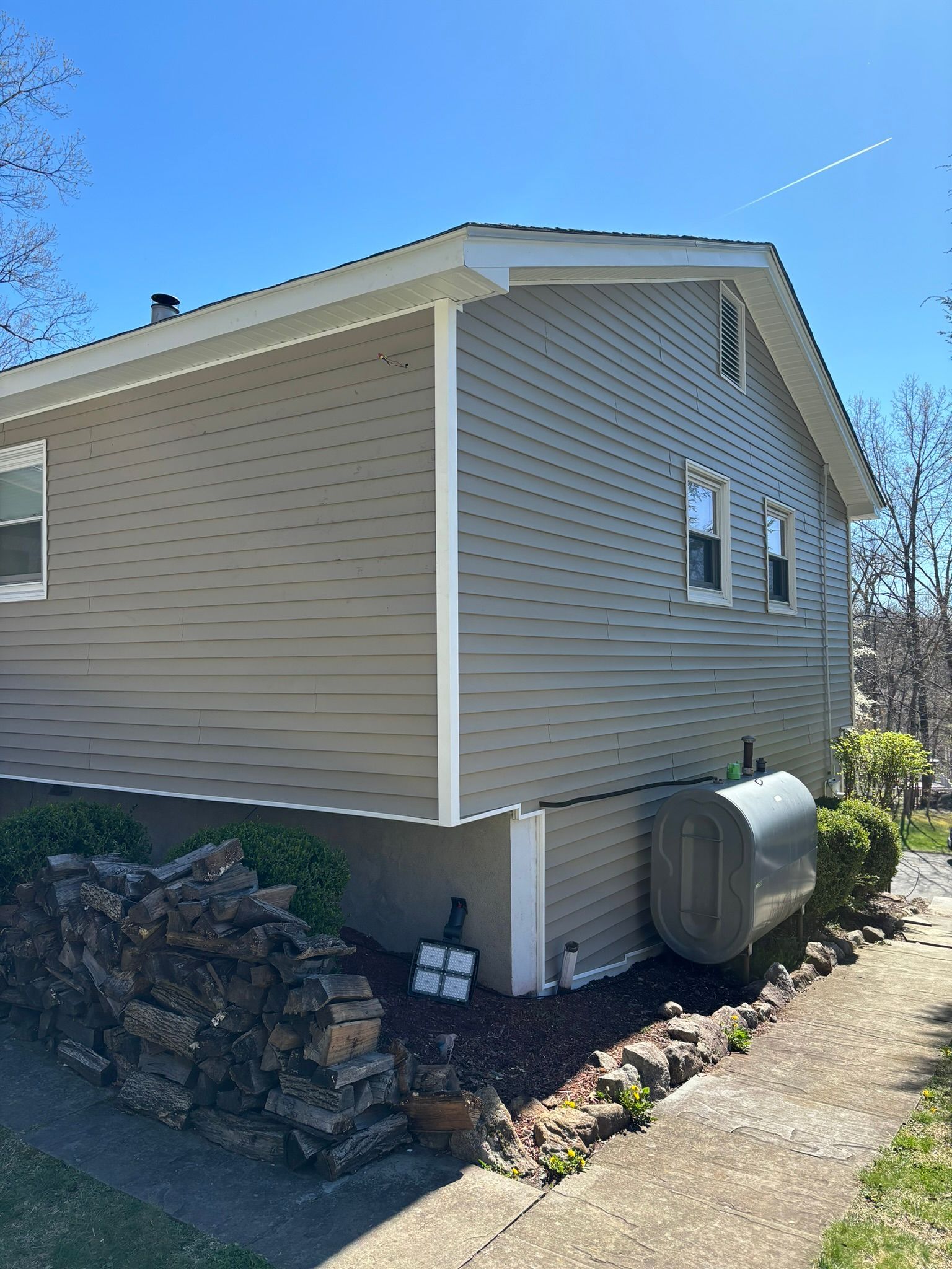 Tan house with white trim, gray siding, fuel tank, rock border, and concrete path.