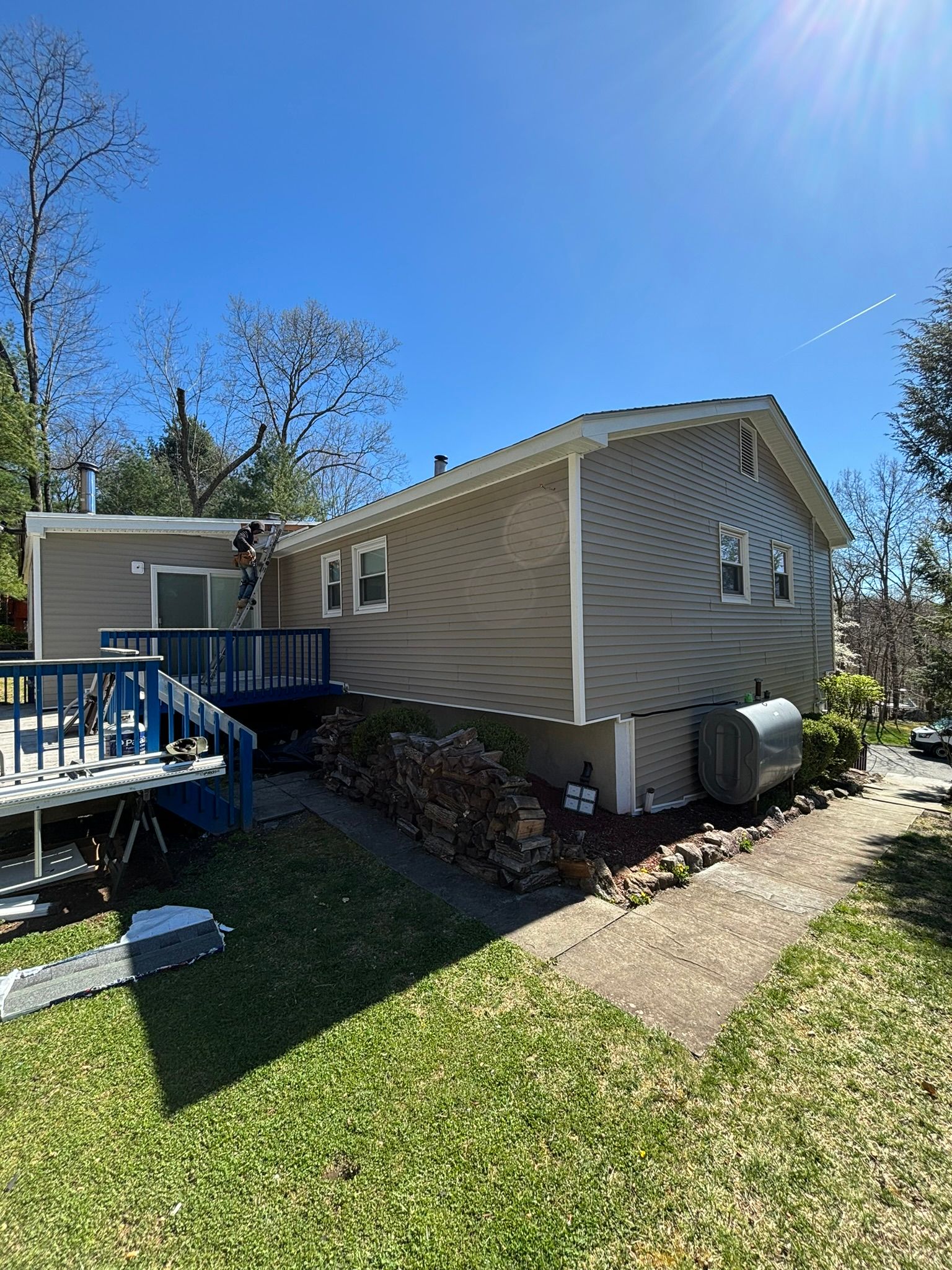 Side view of a two-story house with a deck and a pathway. Green grass and blue sky.