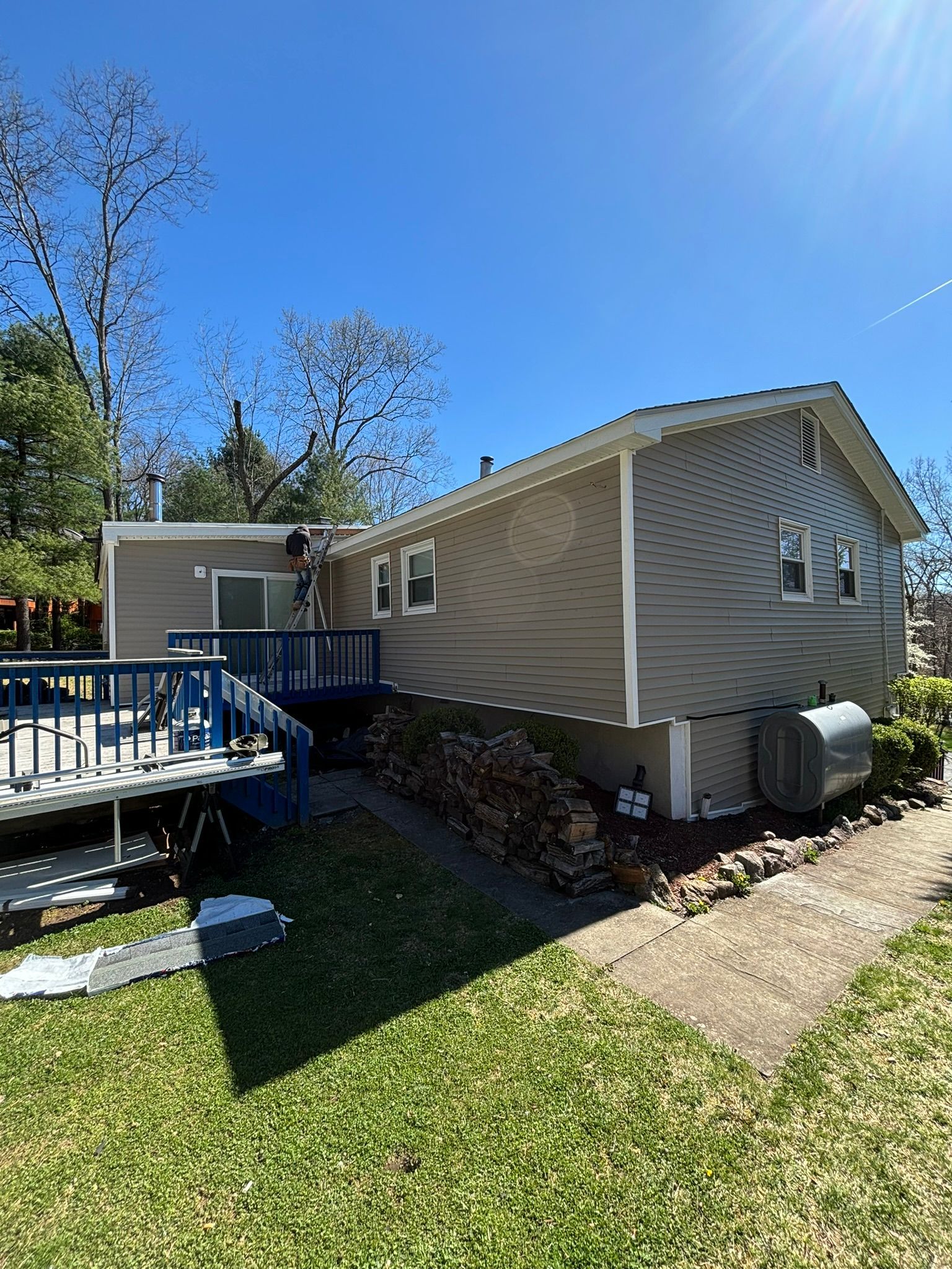 A house with gray siding, blue deck, and a sunny blue sky background.