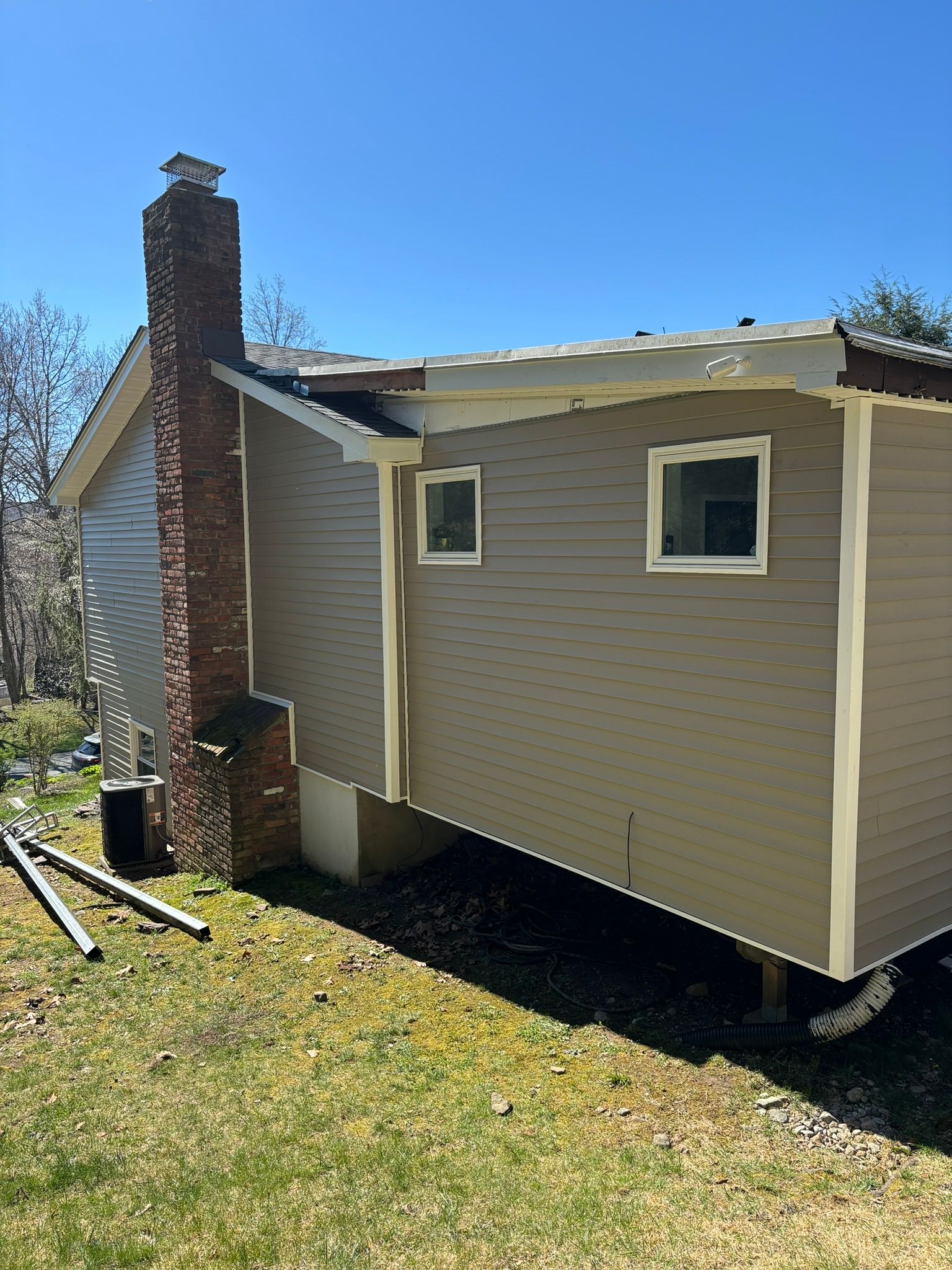 Side view of a house with brick chimney and beige siding, under a clear blue sky.