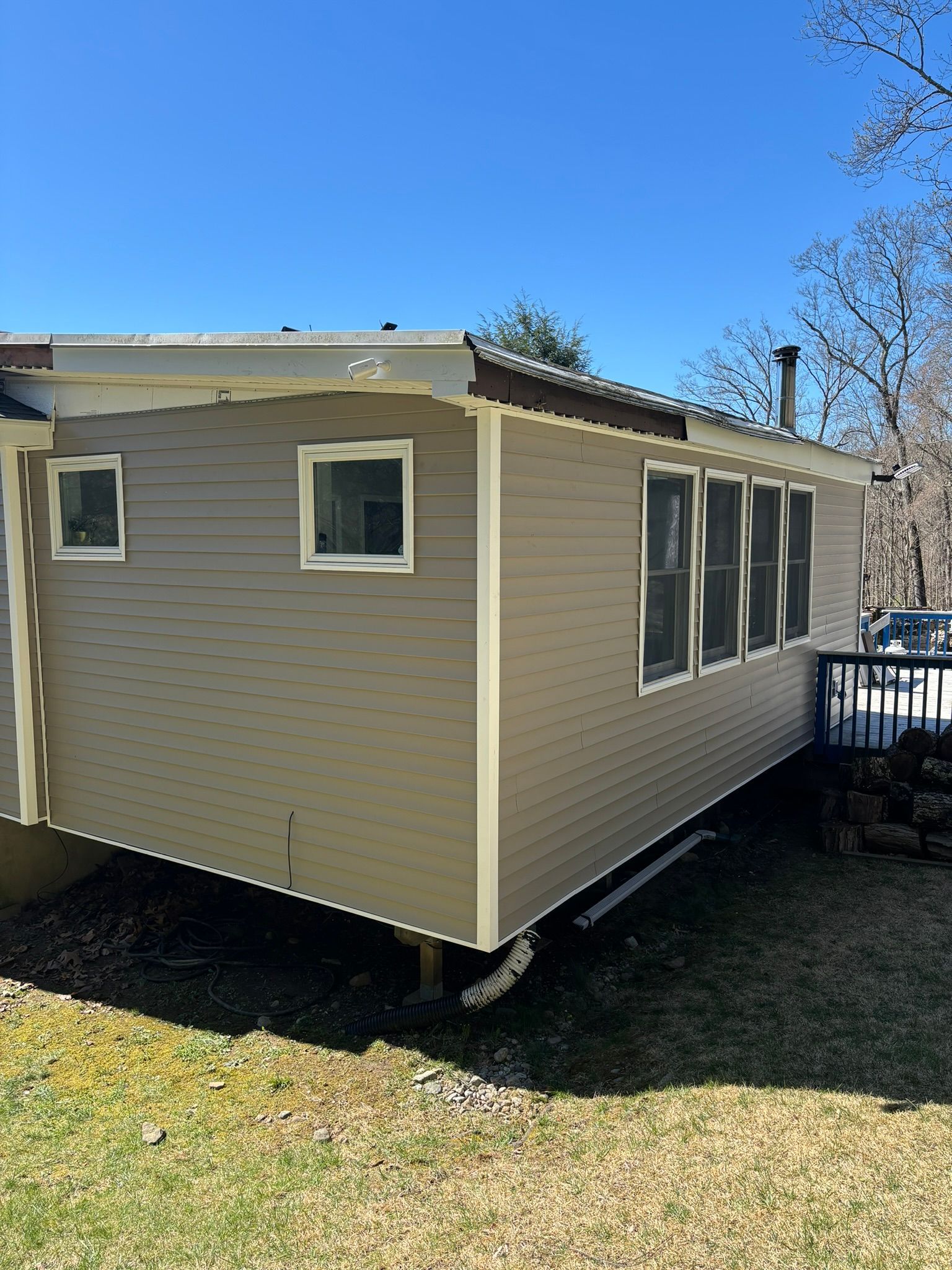Tan-sided house with white trim and multiple windows, on a sunny day with a blue sky.