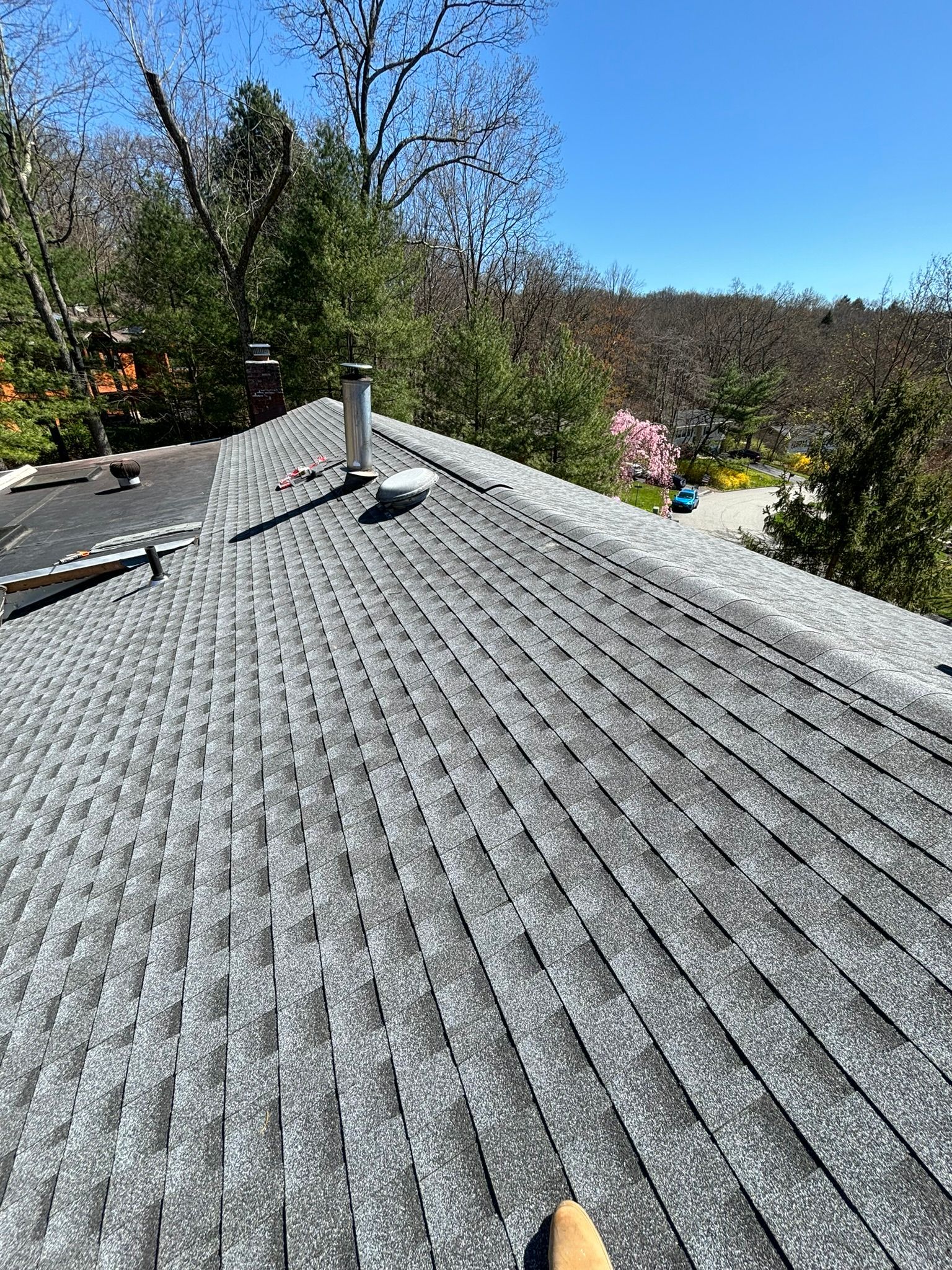 Gray asphalt shingle roof with a chimney, viewed from above on a sunny day.