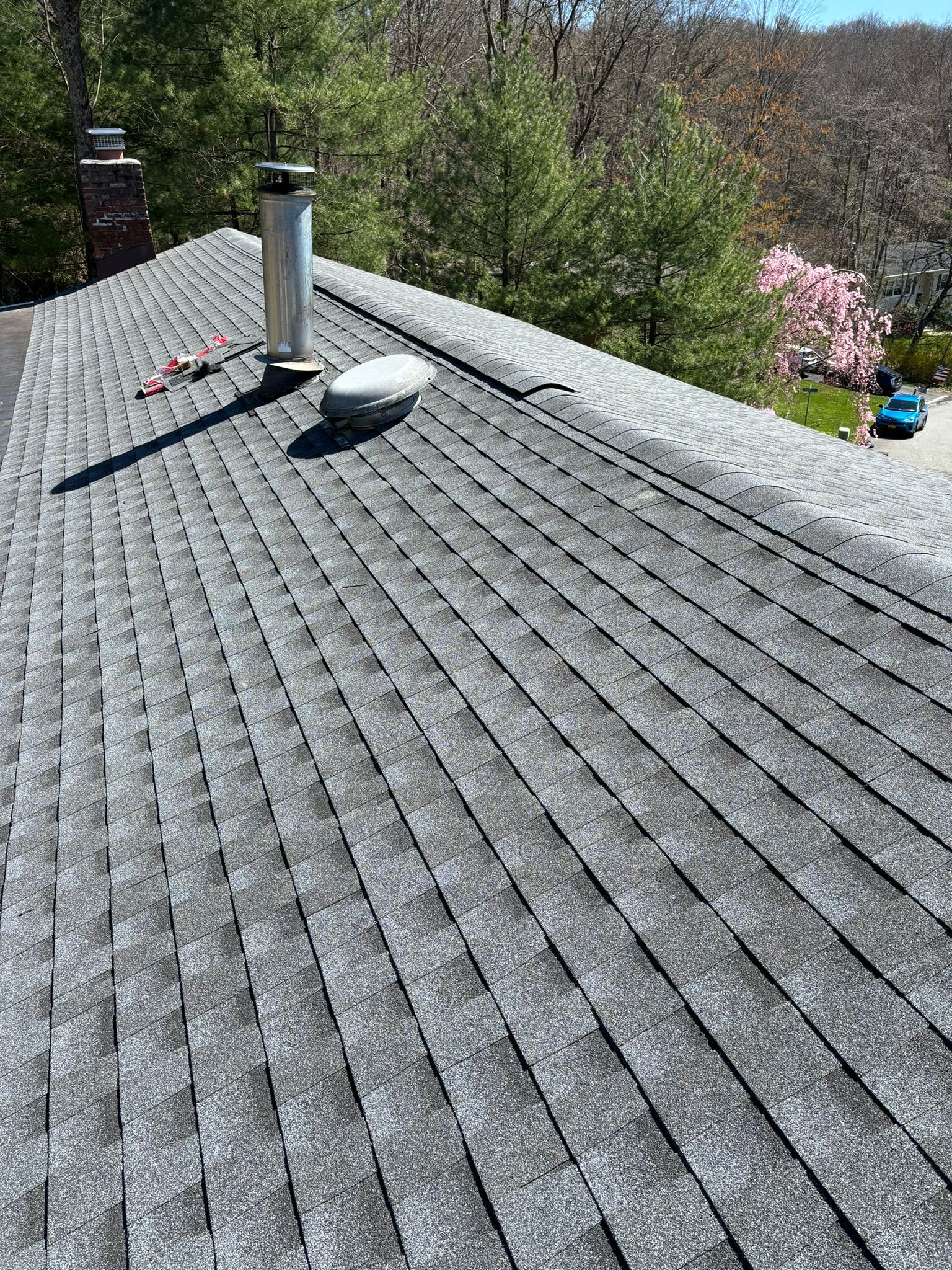 Gray asphalt shingle roof with metal vents, chimney, and scattered debris under a sunny sky.