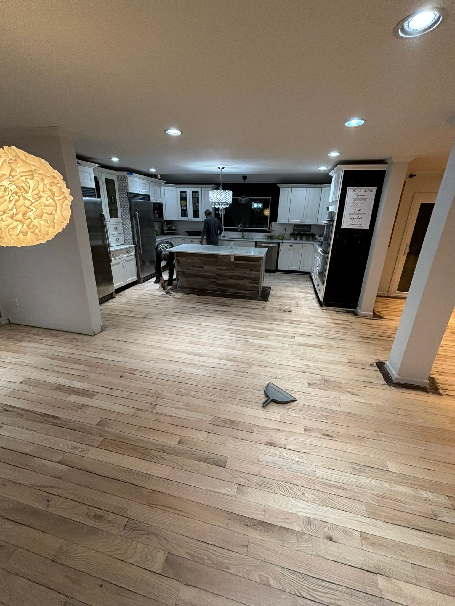 A kitchen with new light wood floors and white cabinets; construction in progress.