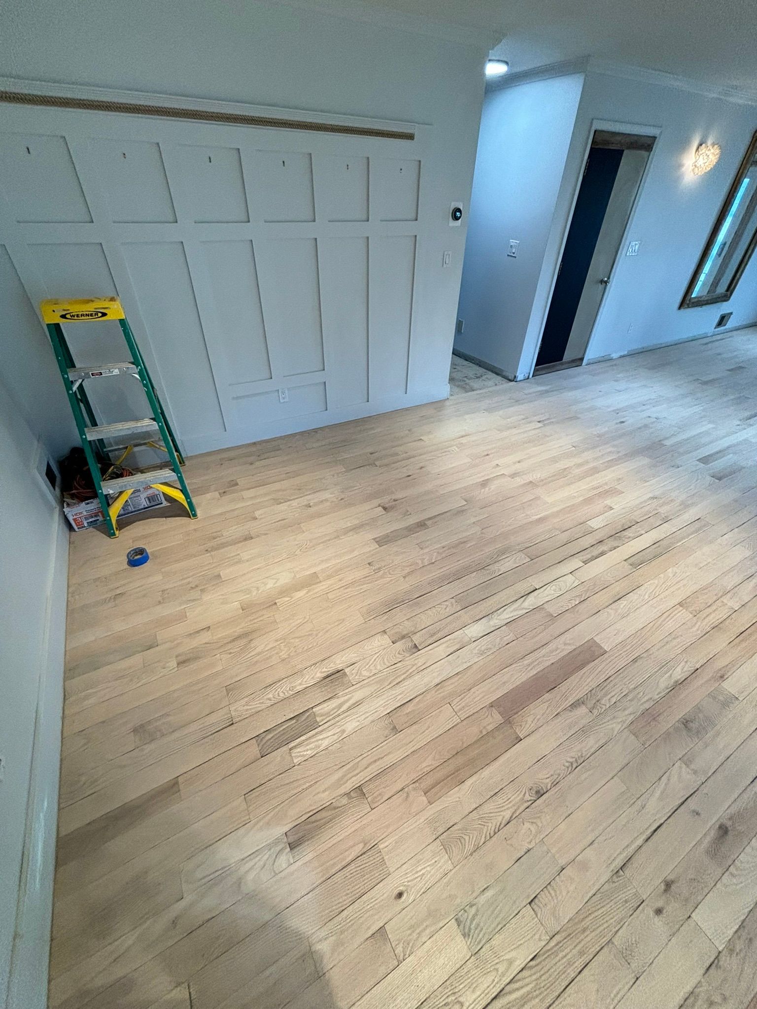 Light wood floor in a room with light blue walls, a ladder, and paneling.