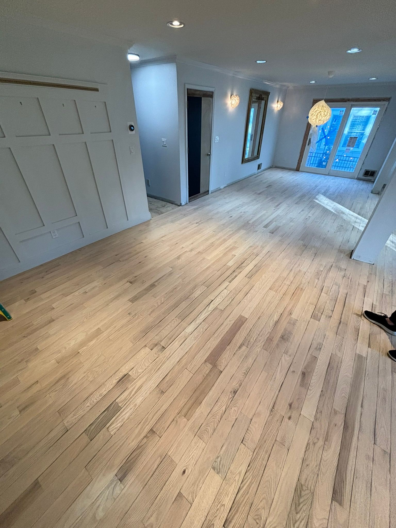 Newly installed light-colored hardwood floors in an empty room with white walls and doorway.