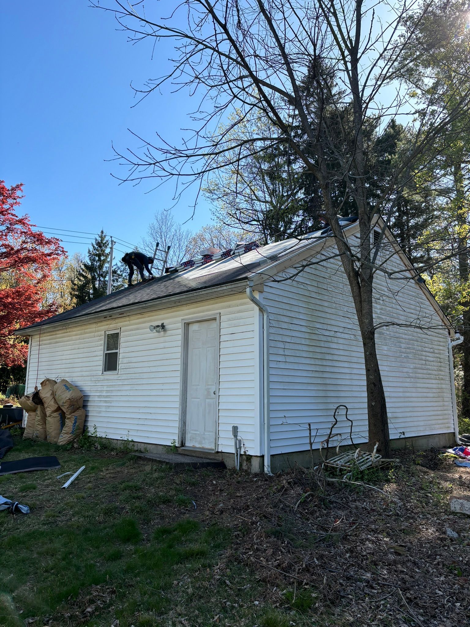 White building with door and window, set against a backdrop of trees and a blue sky.