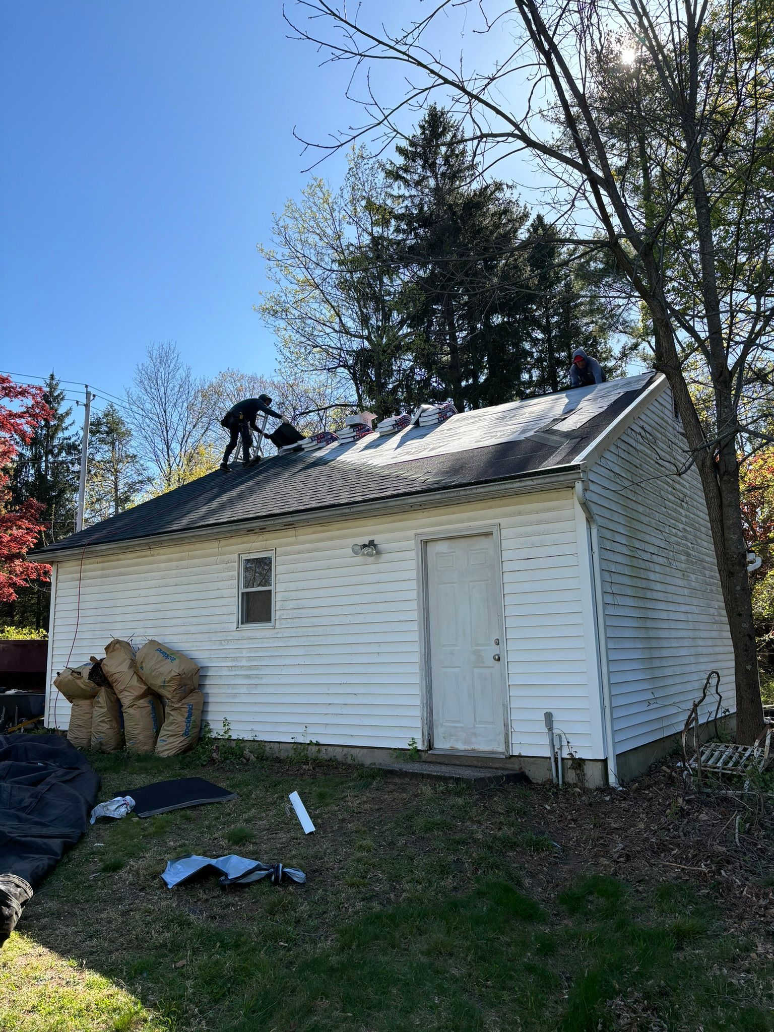 Person replacing roof shingles on a white garage on a sunny day.