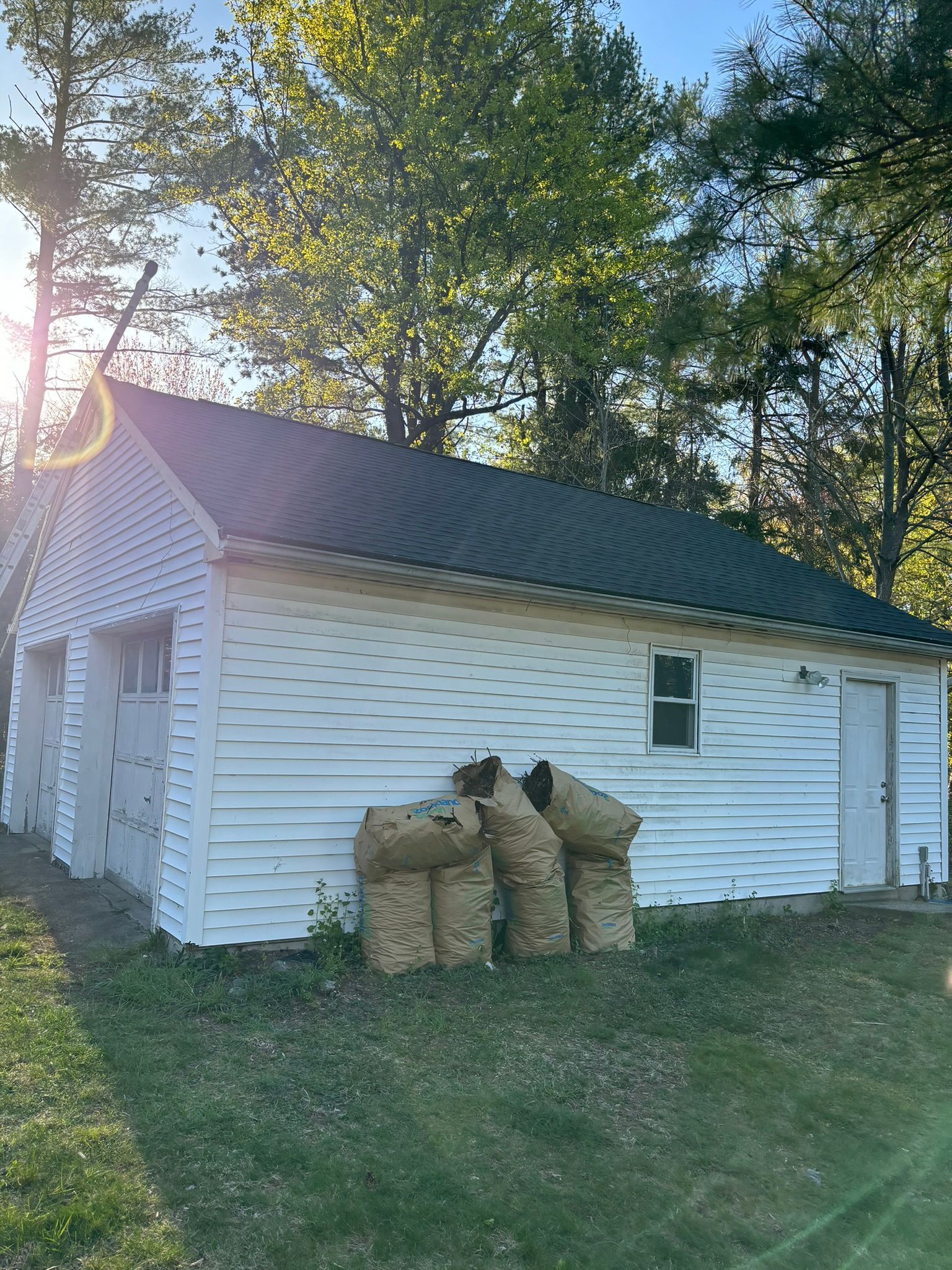 White garage with green roof, three doors, small window, and yard, surrounded by trees.
