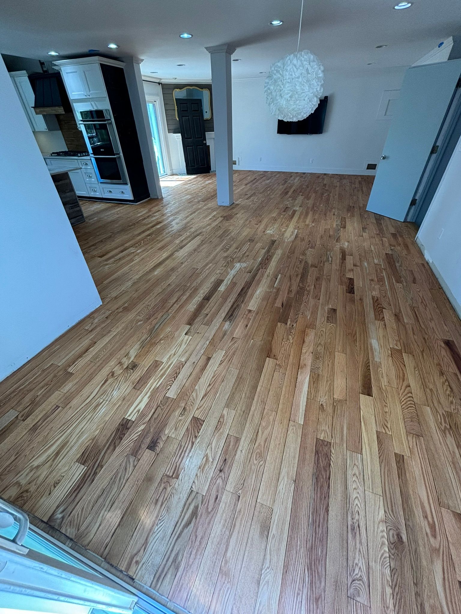Hardwood floors in a room with a kitchen, column, and white walls.