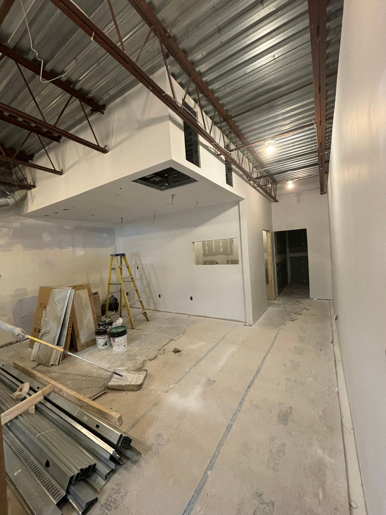 Construction site interior with exposed beams, white walls, and a partially built mezzanine.