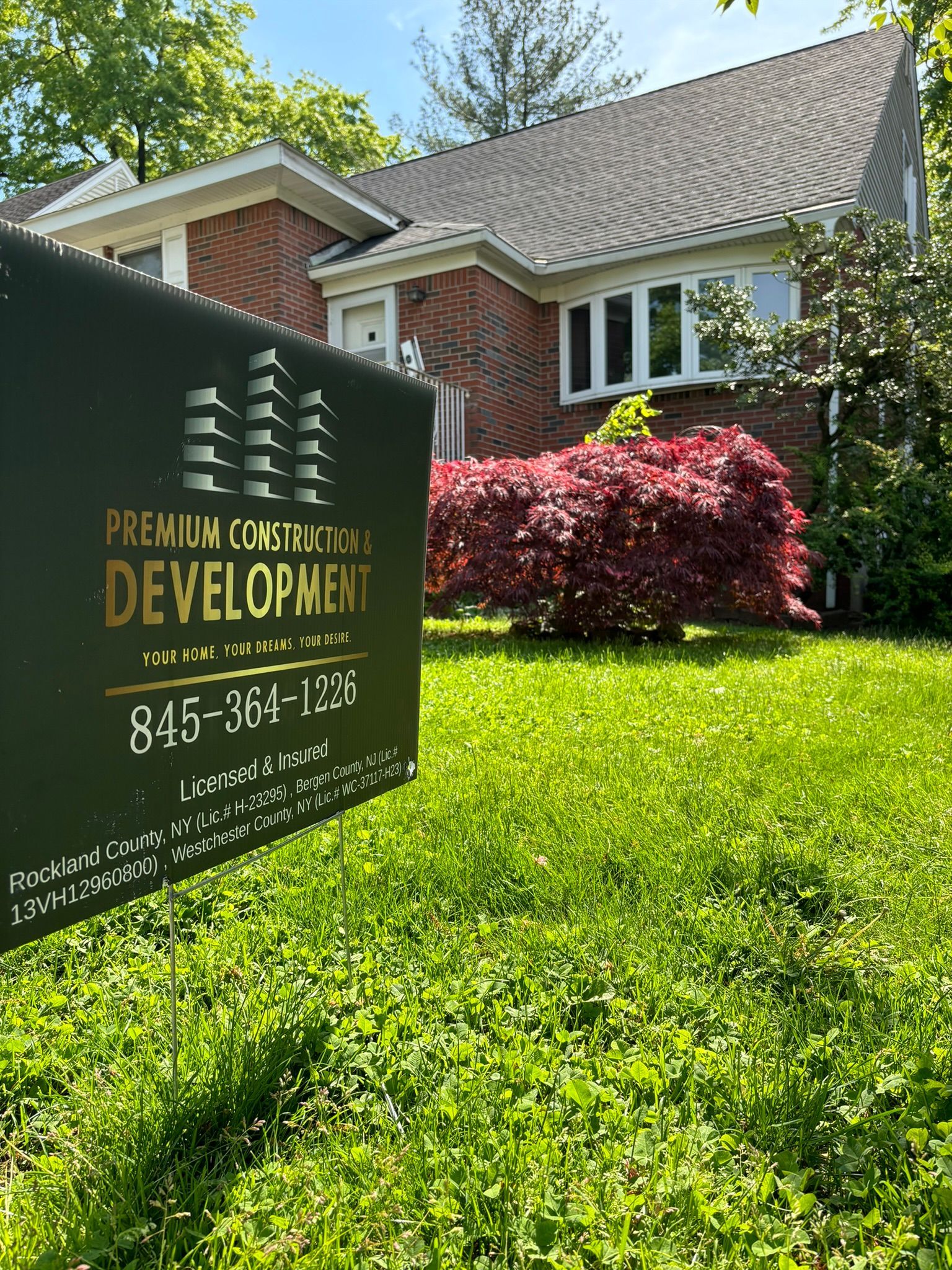 Sign for Premium Construction Development in front of a brick house with green grass and red bushes.