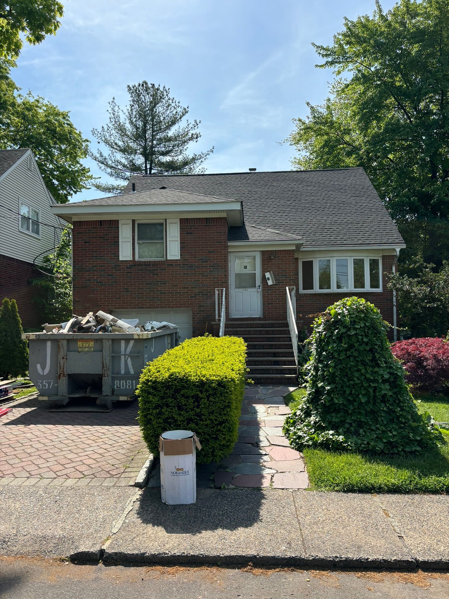 Brick house with dumpster in front, two story, bushes and walkway in front yard.