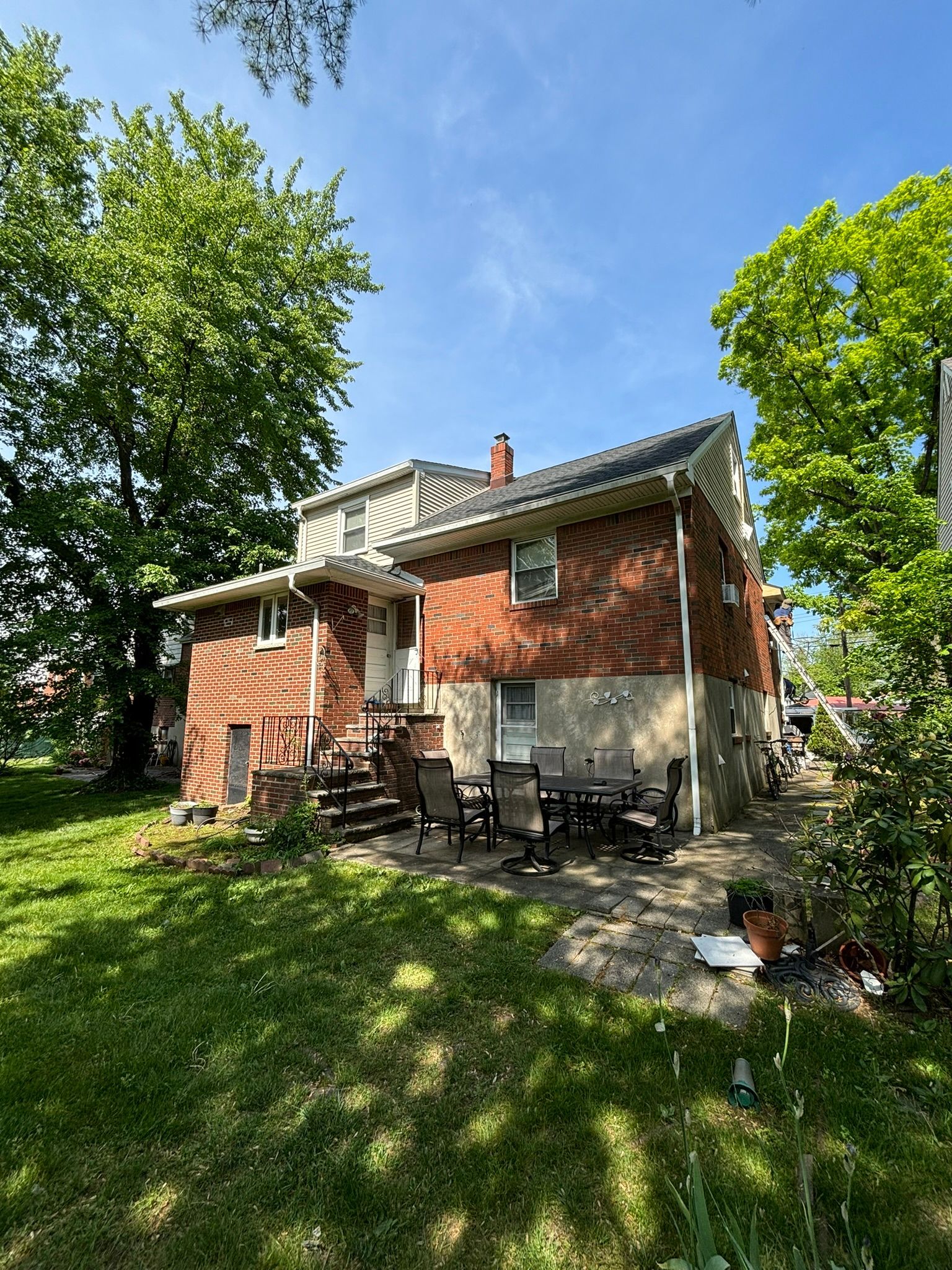 Brick house with a patio, lawn, and trees under a blue sky.