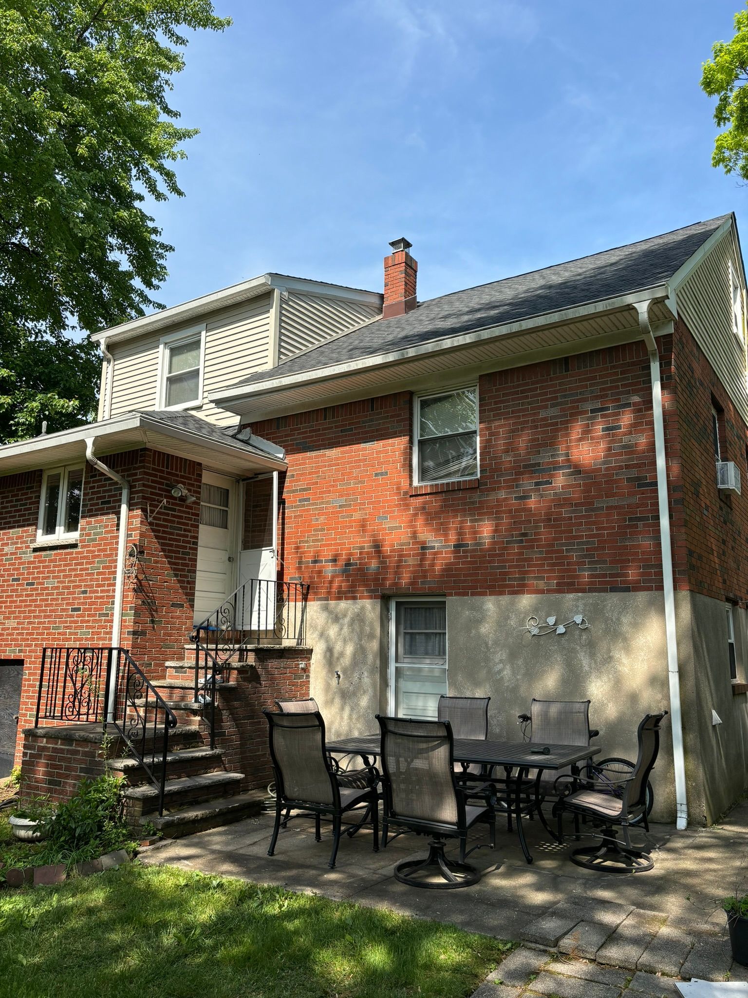 Backyard with a brick house, patio table, chairs, and steps leading to the back door.