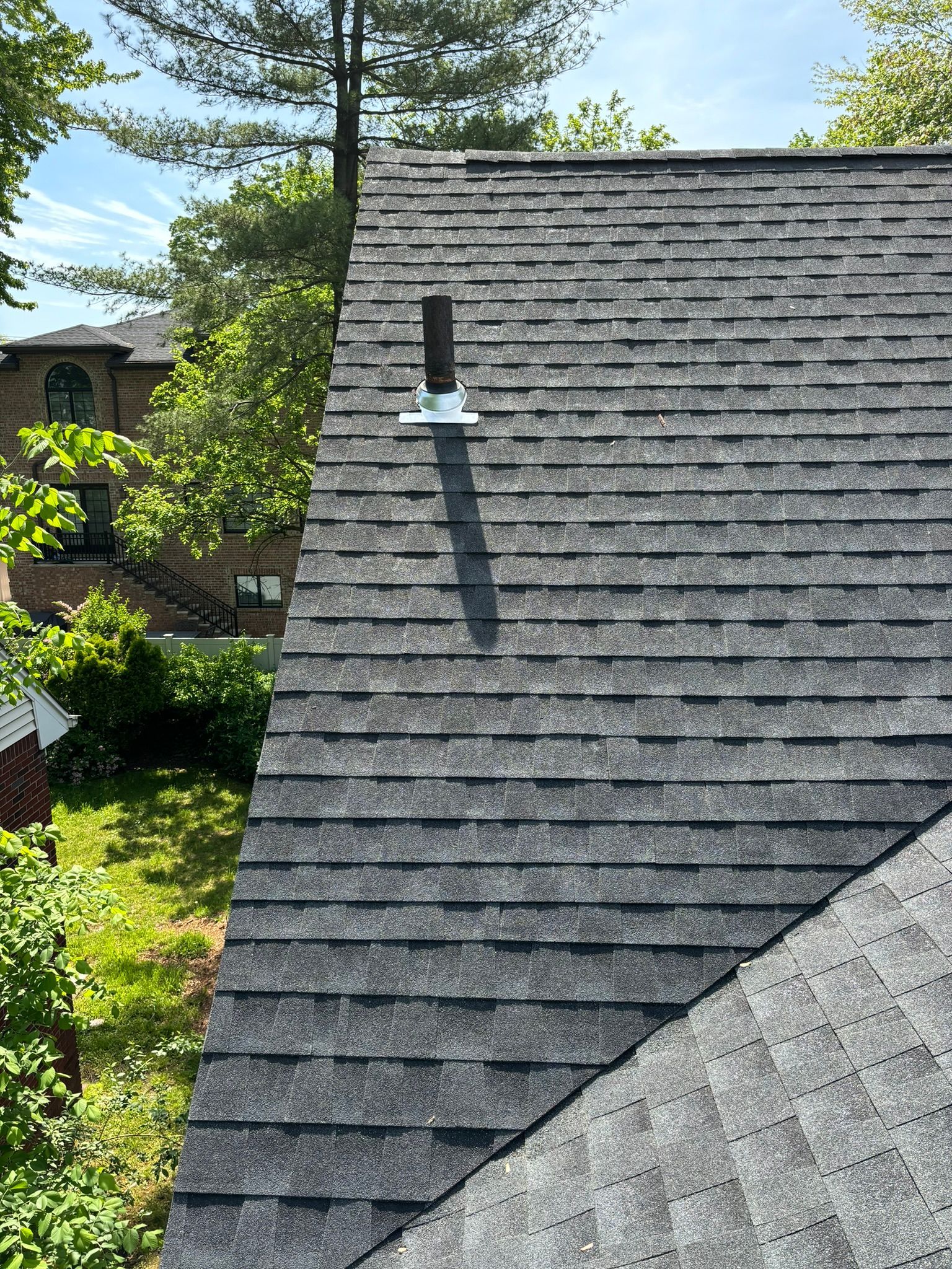 A dark gray shingle roof with a vent pipe. Green trees and a building are in the background.