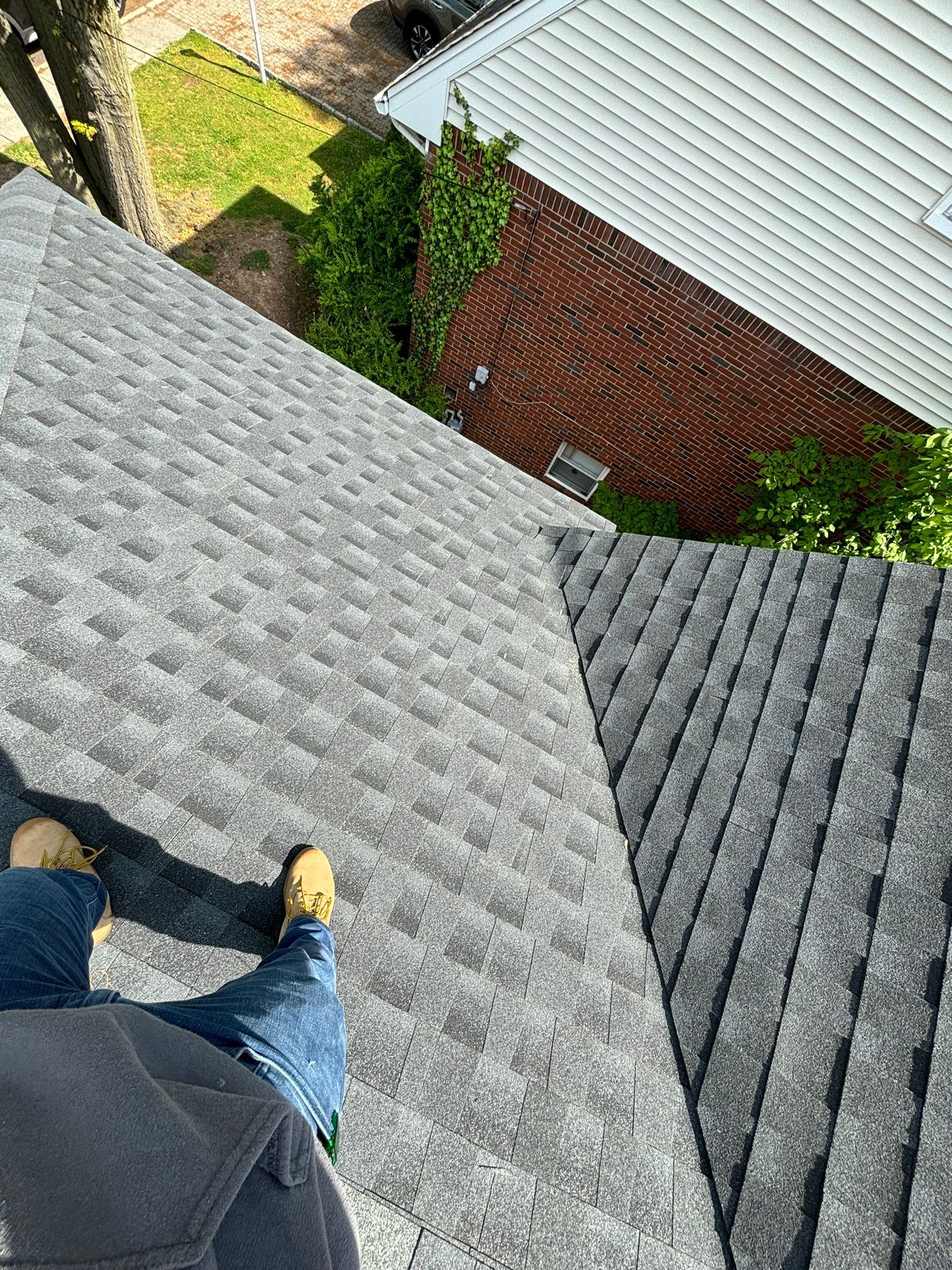 Person on a gray shingle roof; looking down at a brick building and lawn.