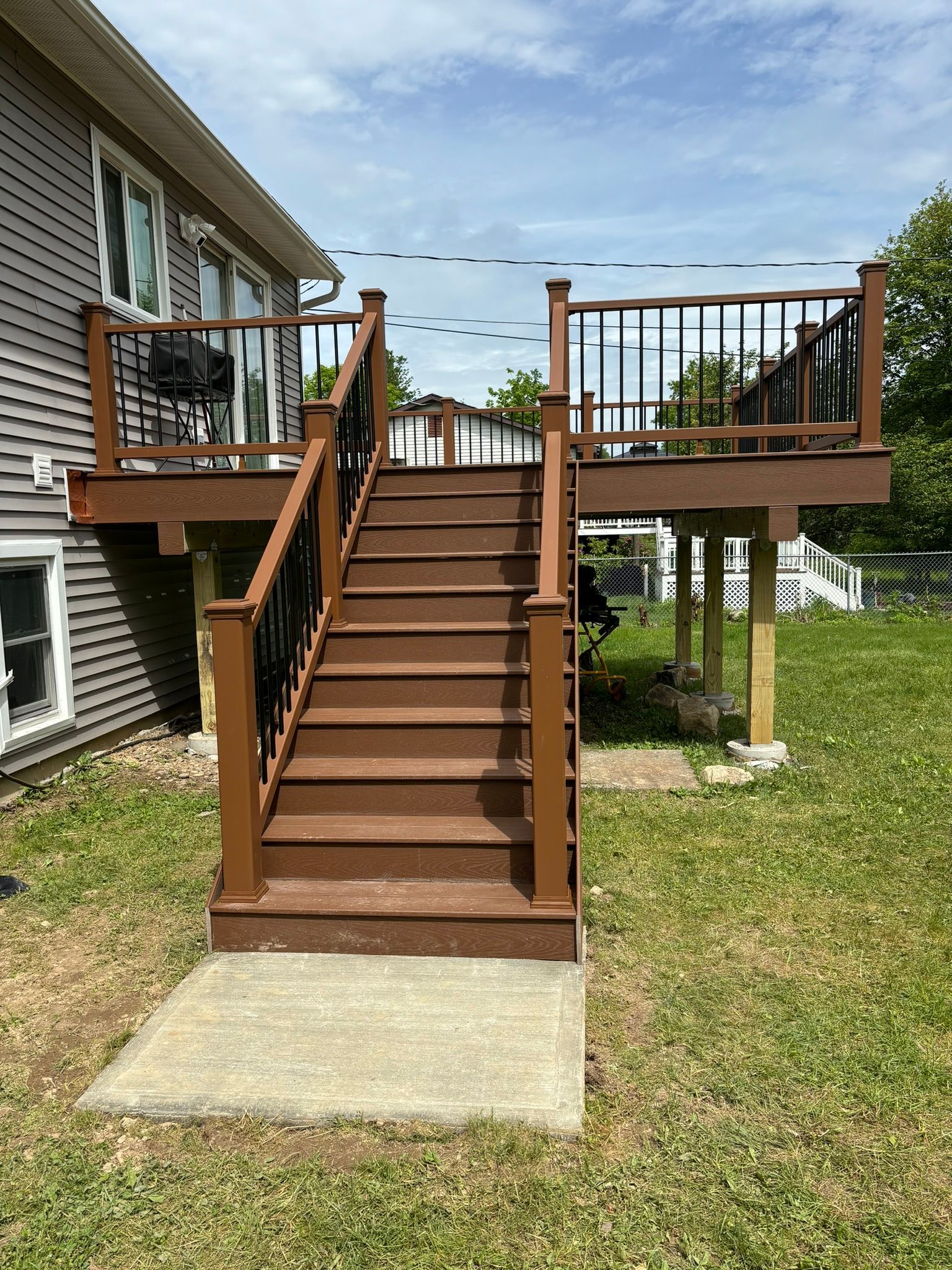 Brown composite deck with steps leading up from a concrete pad in a grassy yard.