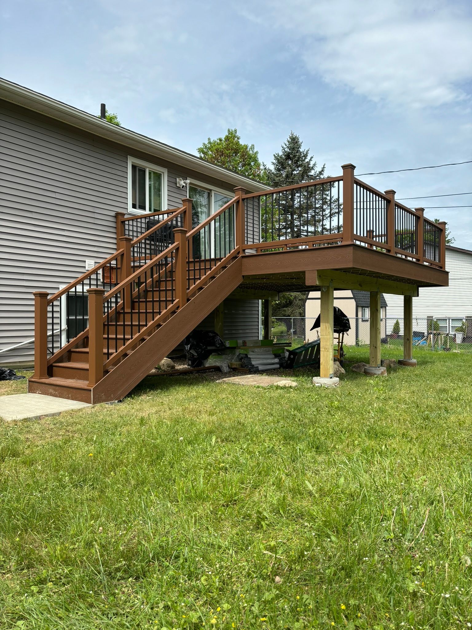 Brown deck with stairs, overlooking a grassy yard. The deck has a black and clear railing.