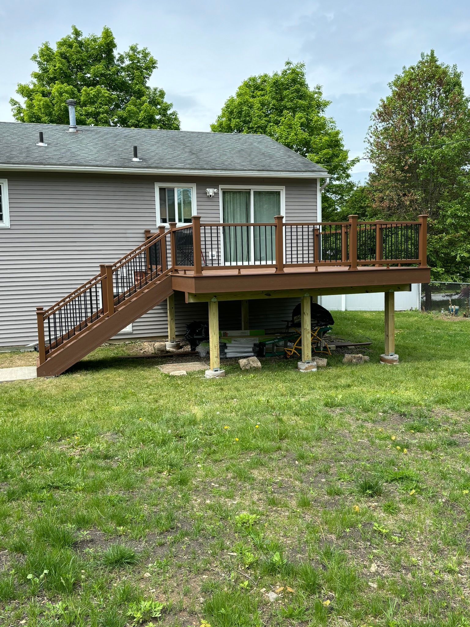 Wooden deck with stairs attached to a gray house, viewed from a grassy yard on a cloudy day.