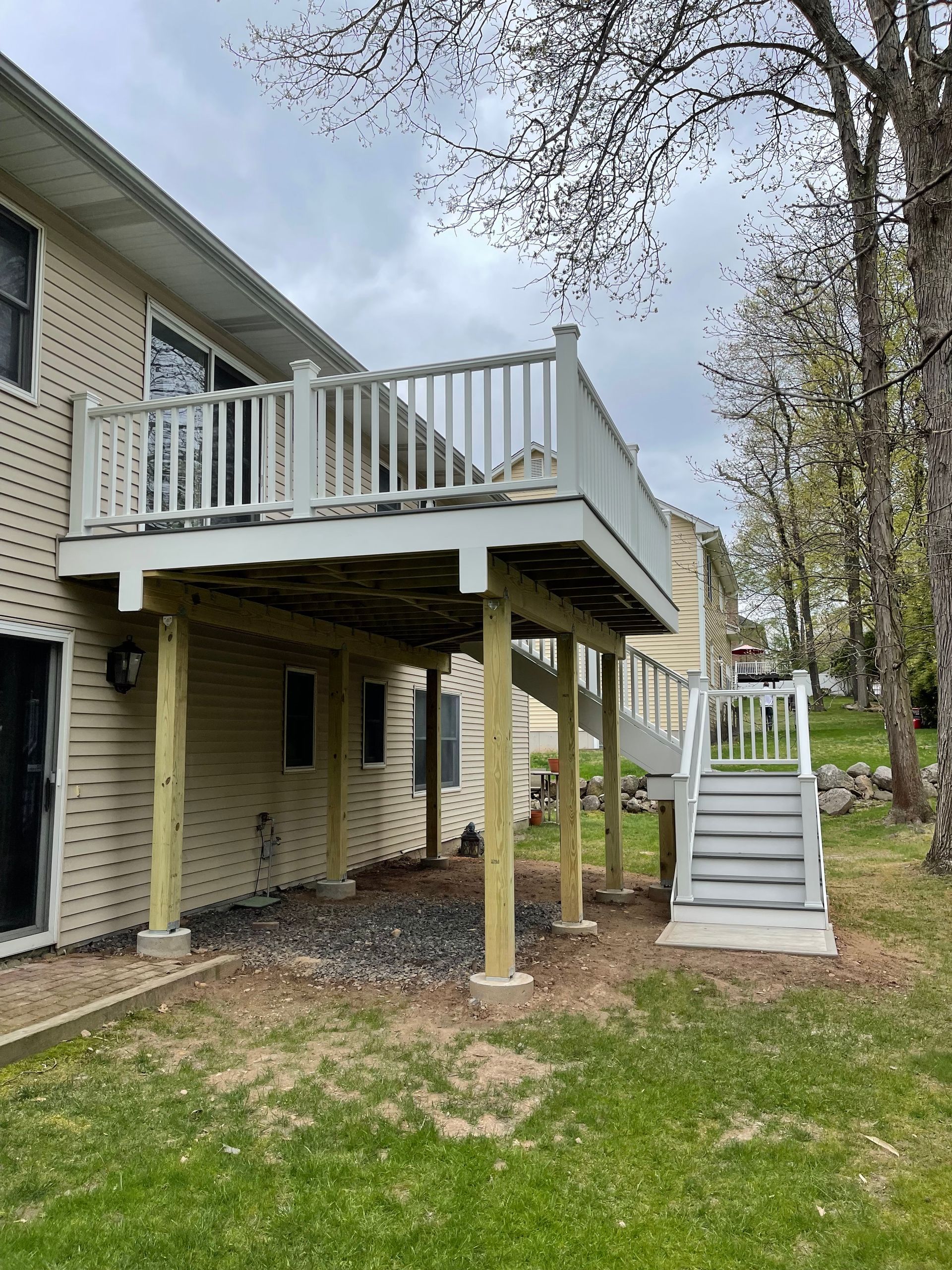 Two-story deck attached to a beige house with stairs and wooden supports. Gray sky overhead.